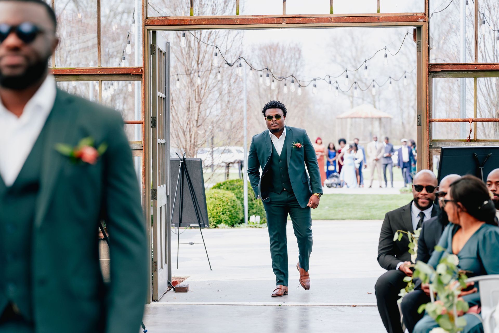 A man in a green suit is walking down the aisle at a wedding.