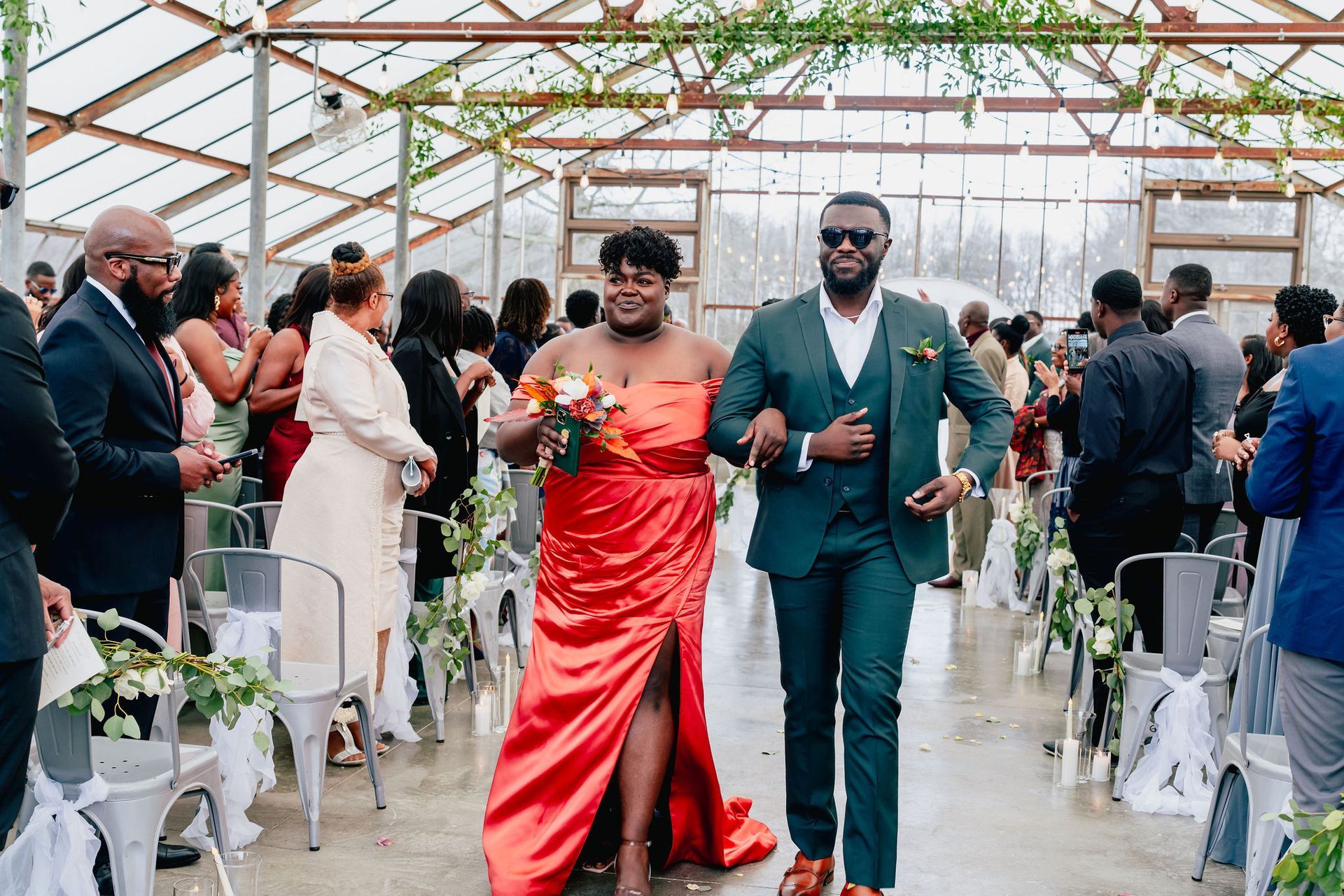 A bride and groom are walking down the aisle at their wedding in a greenhouse.