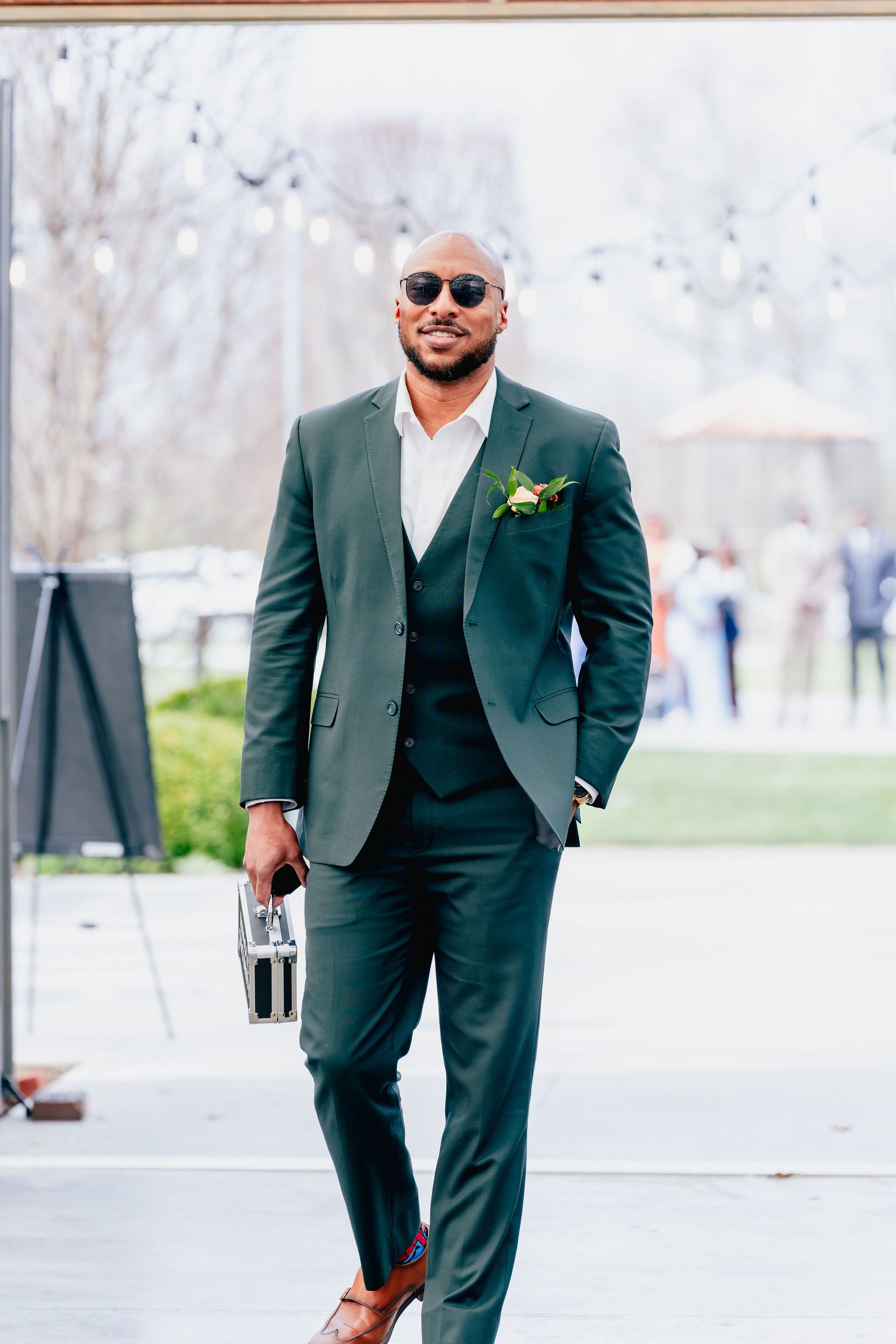 A man in a green suit and sunglasses is walking down the street.