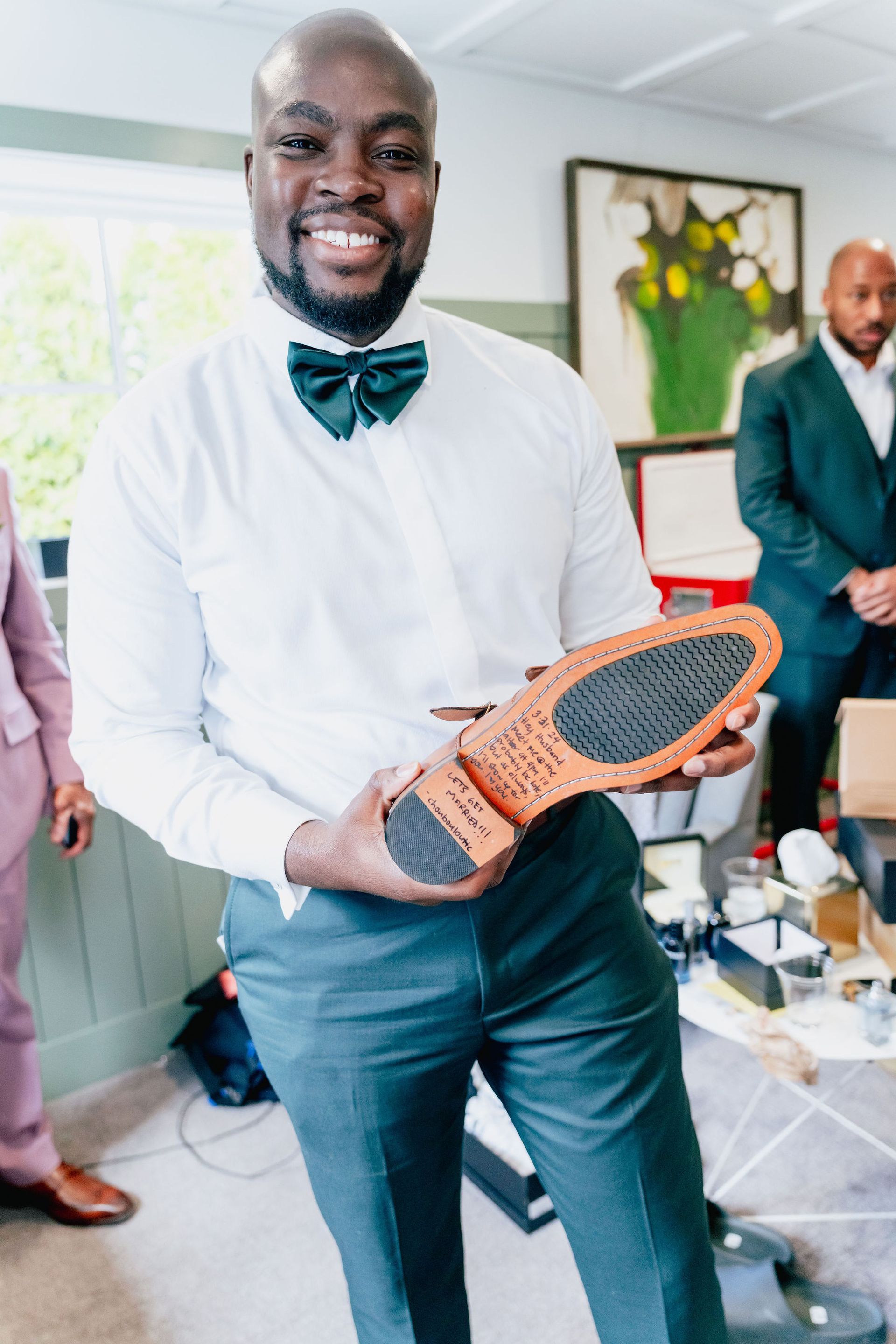 A man in a bow tie is holding a pair of shoes.