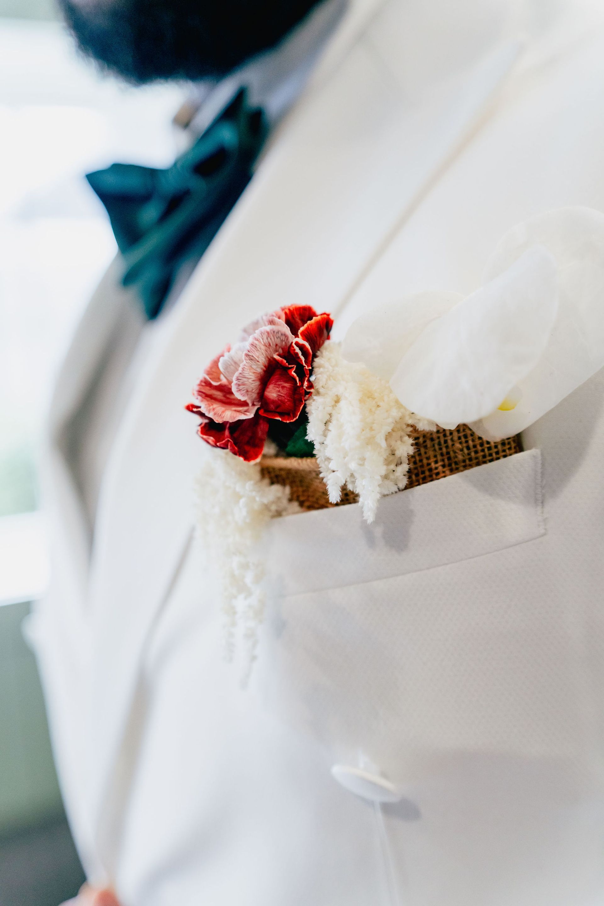 A man in a white suit has a red flower in his pocket.