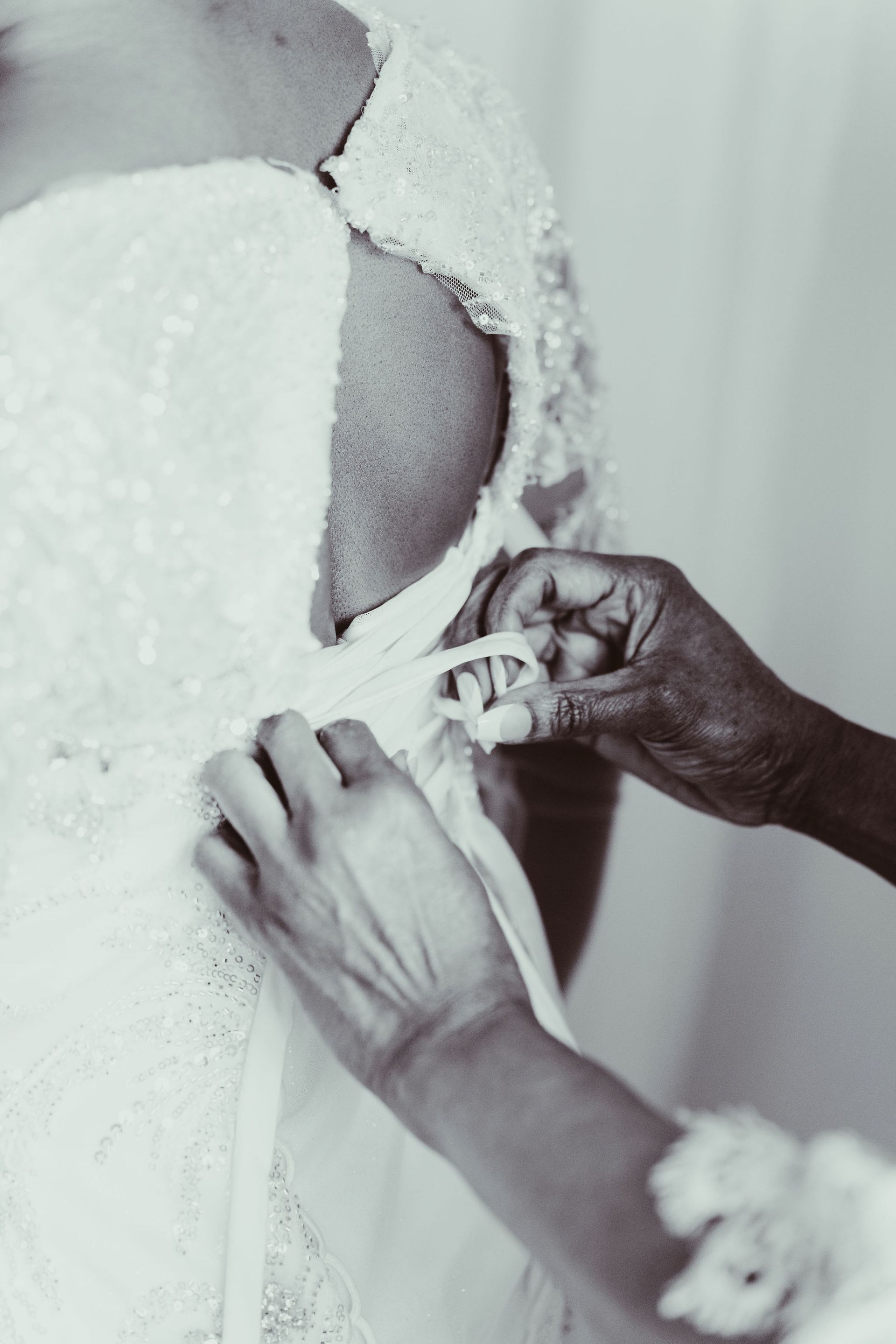 A woman is helping a bride get ready for her wedding in a black and white photo.