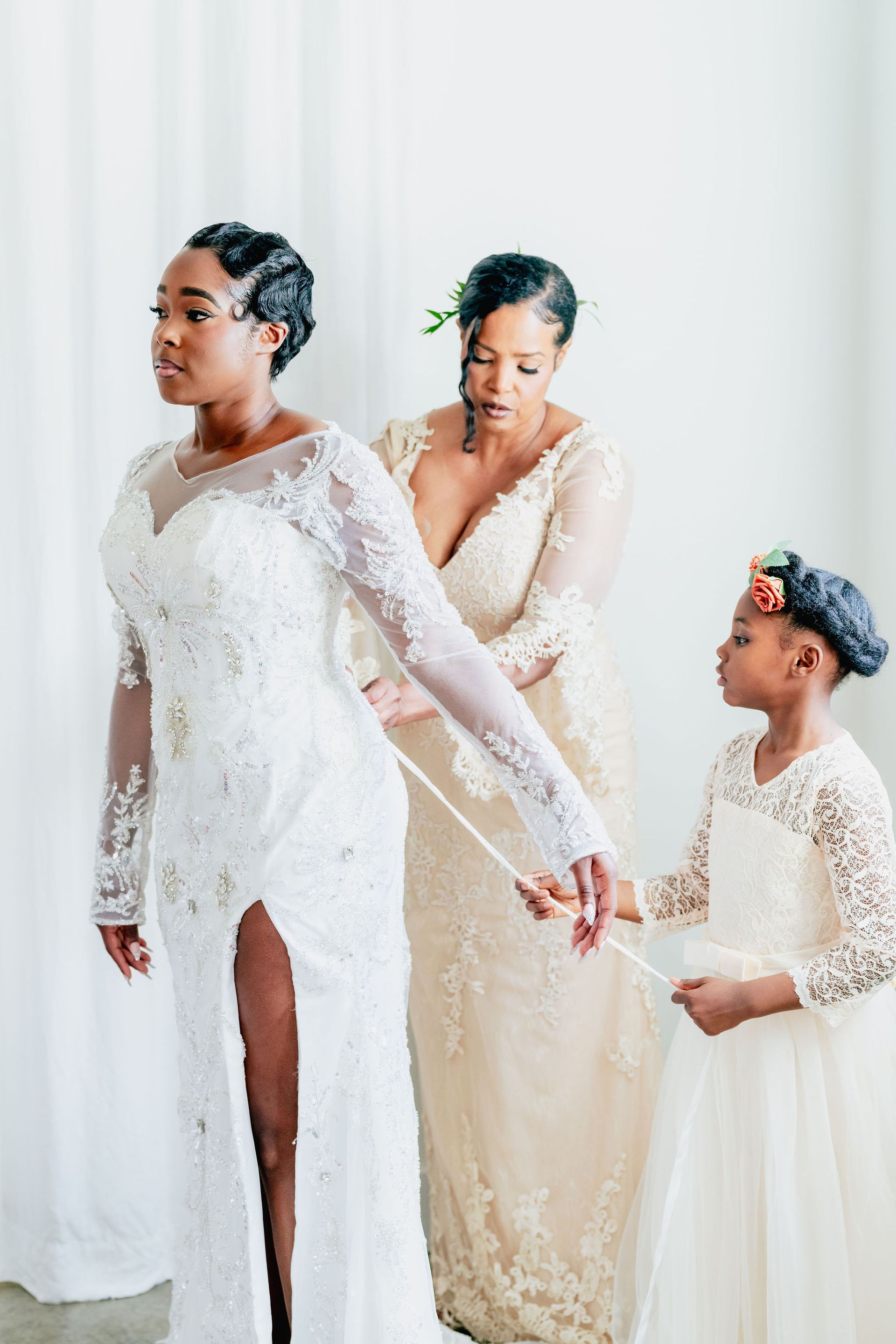 A woman in a wedding dress is being helped by two women and a flower girl.