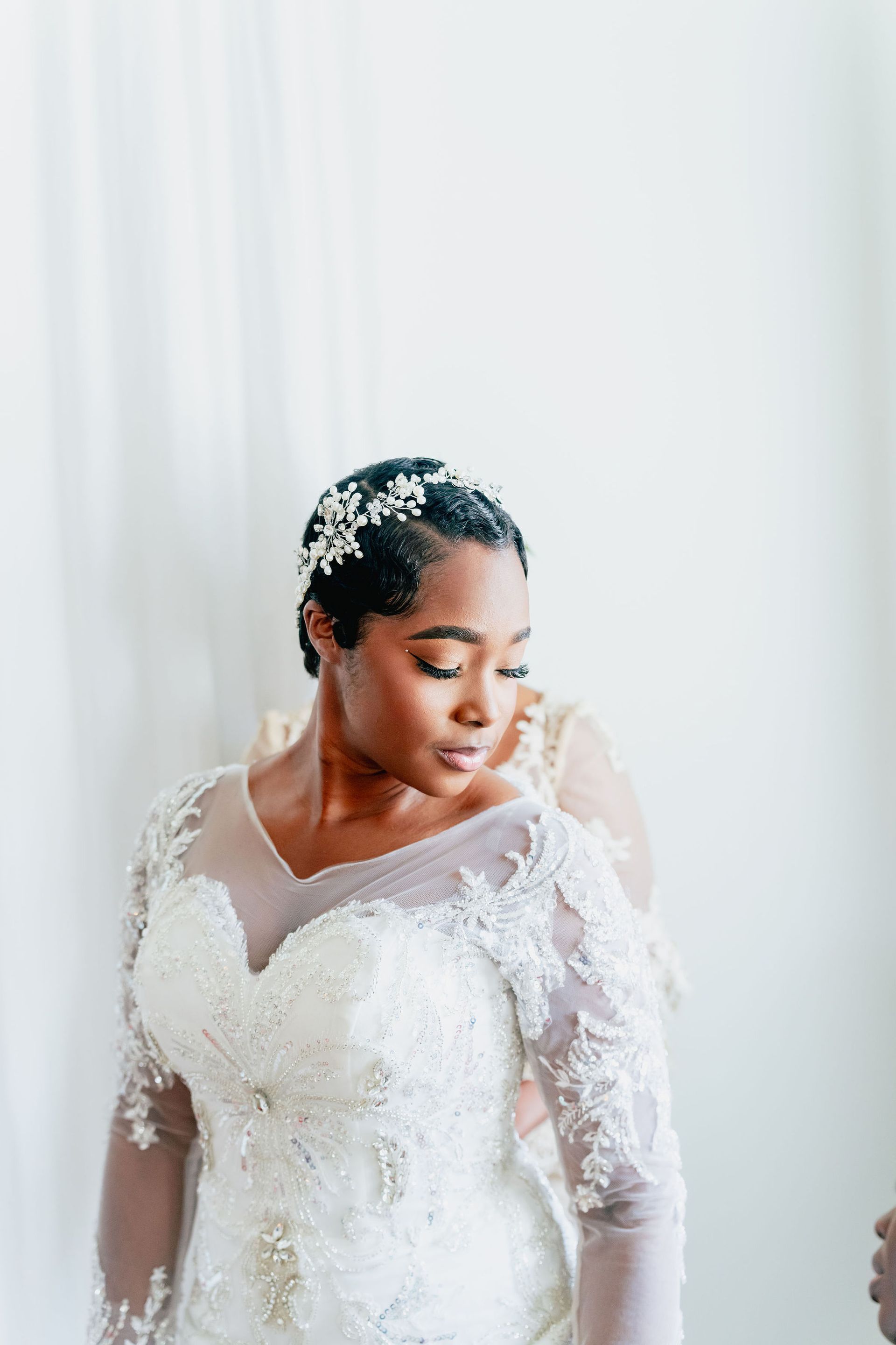A woman in a wedding dress is standing in front of a window.