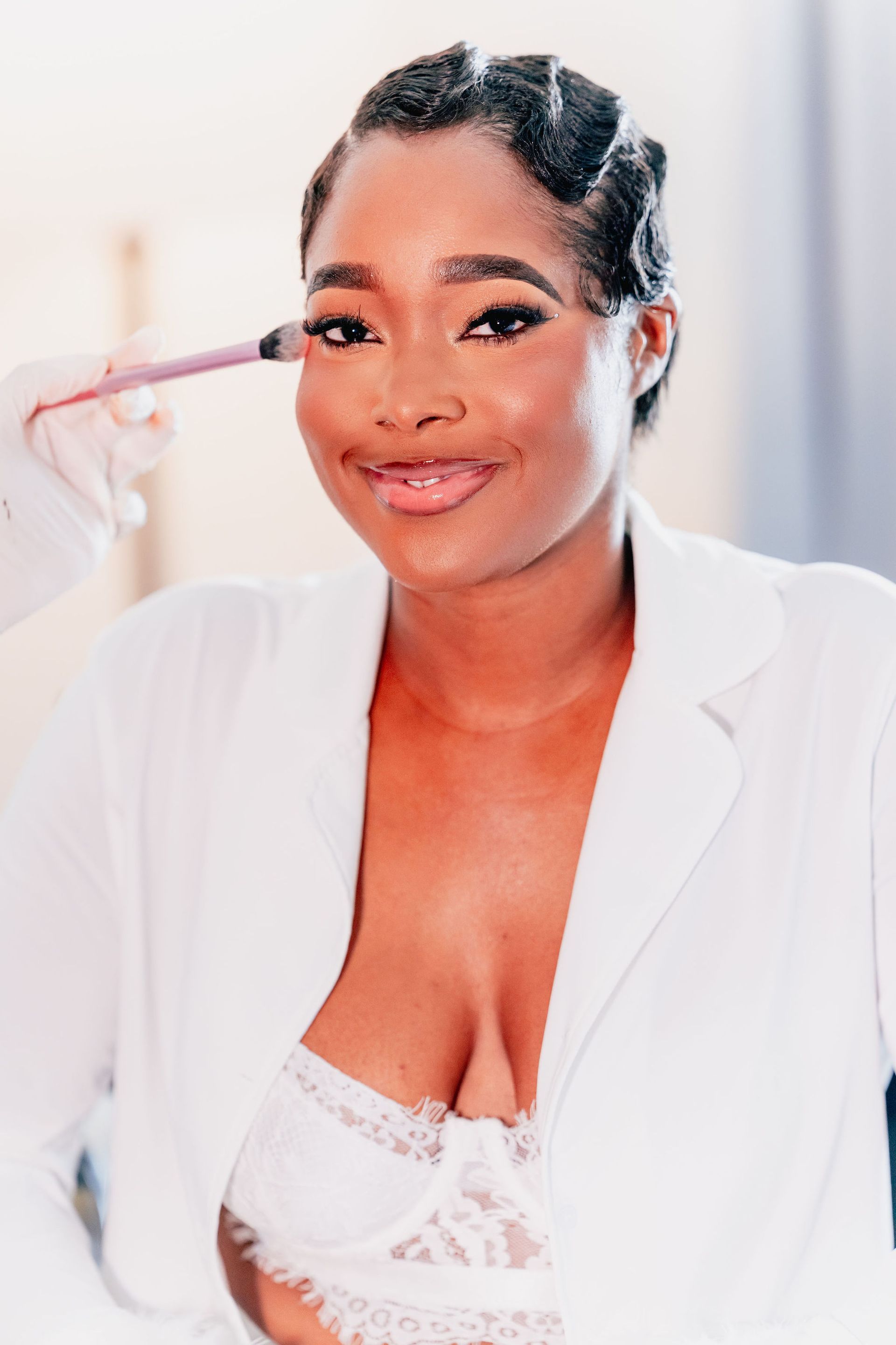 A woman in a white jacket is getting her makeup done.