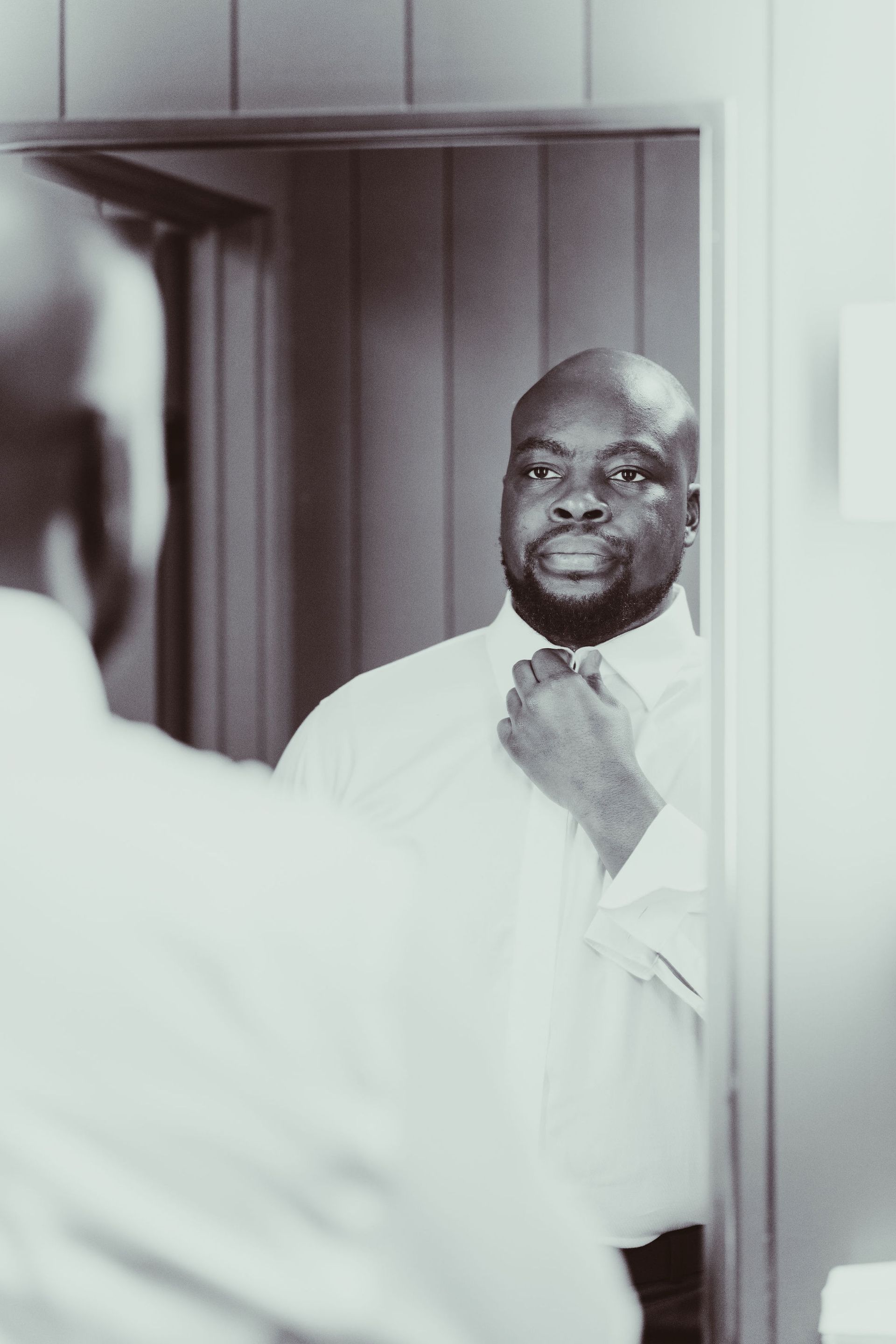 A man is adjusting his tie in front of a mirror.