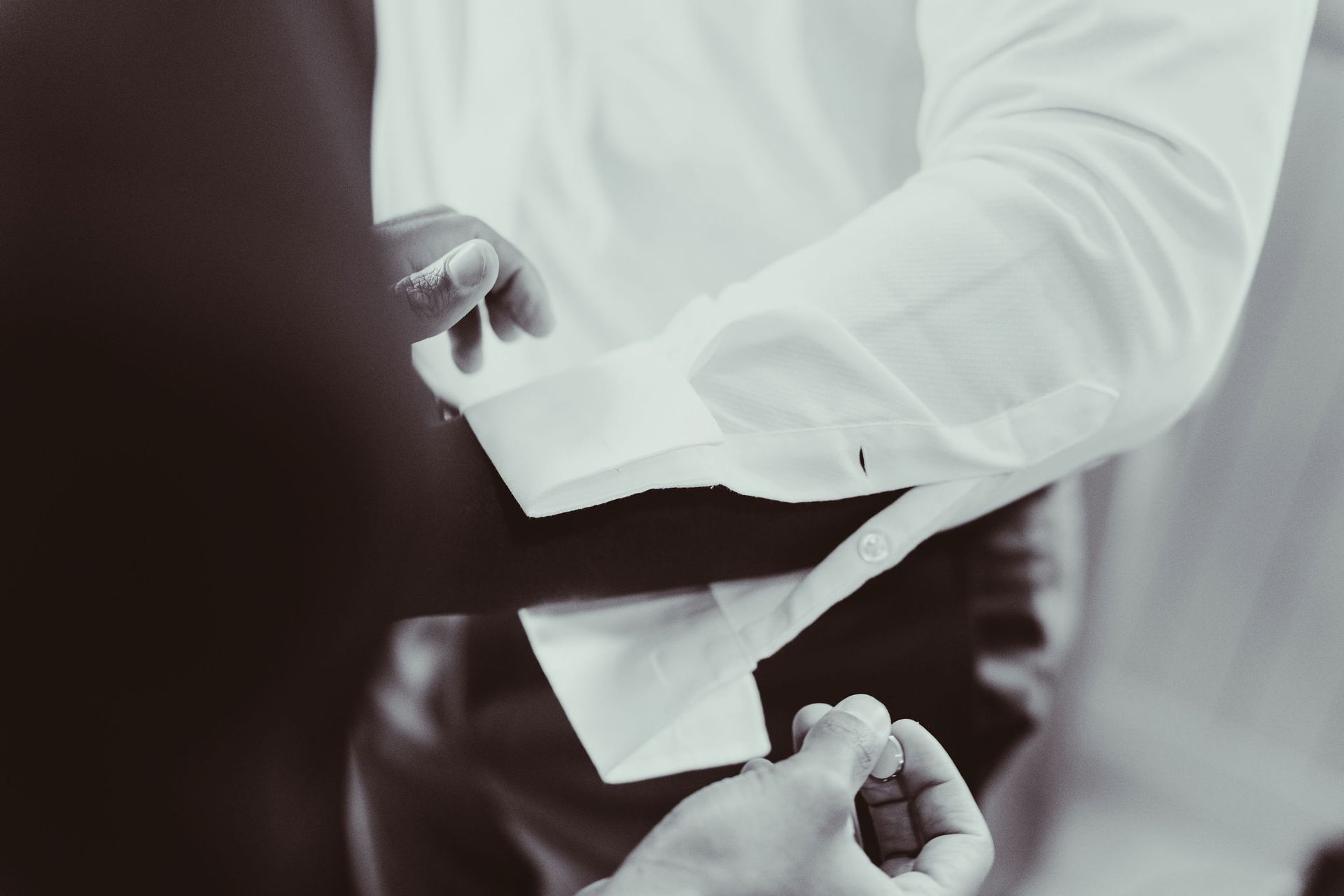 A man is getting ready for a wedding by adjusting his cufflinks.