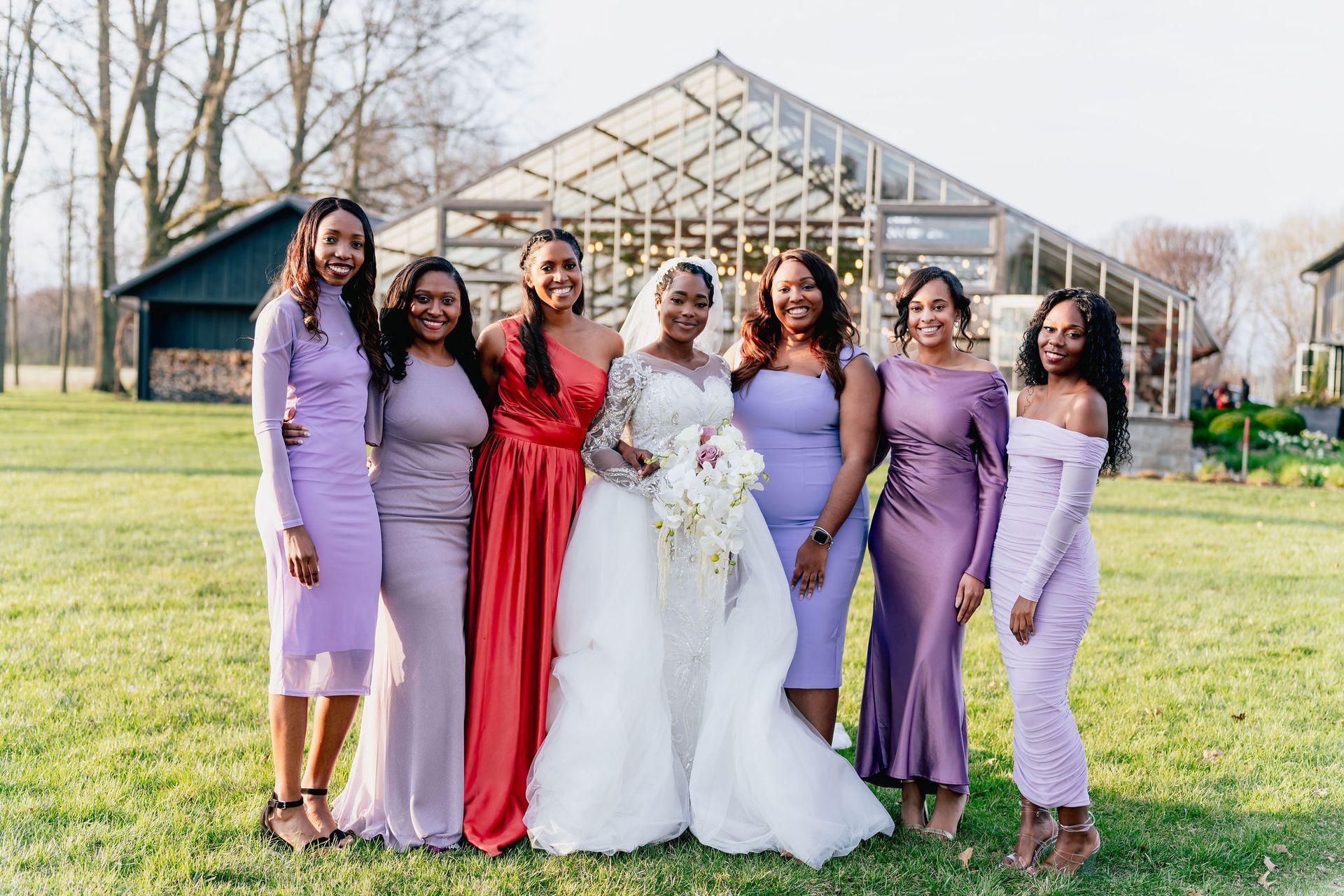 A bride and her bridesmaids are posing for a picture in front of a greenhouse.