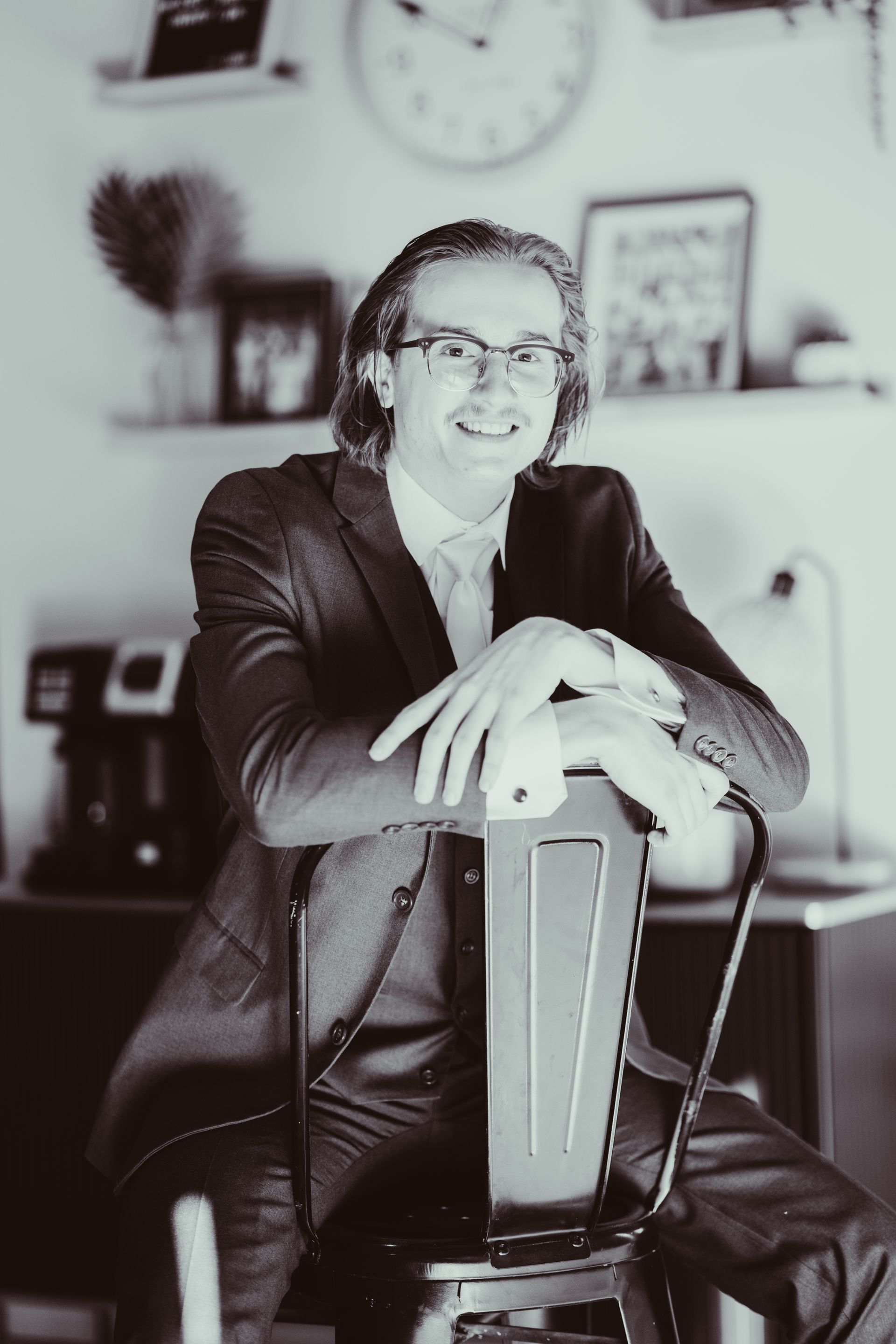 A man in a suit and tie is leaning on a chair.