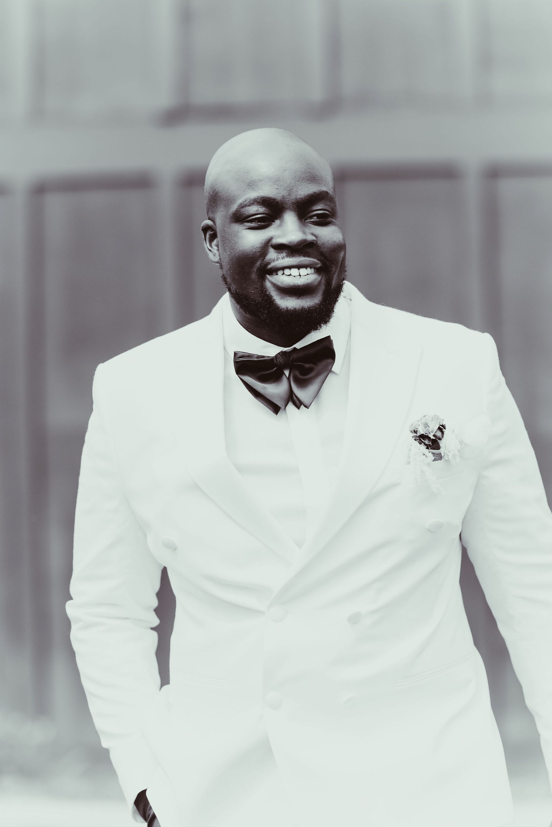 A man in a white suit and bow tie is smiling in a black and white photo.