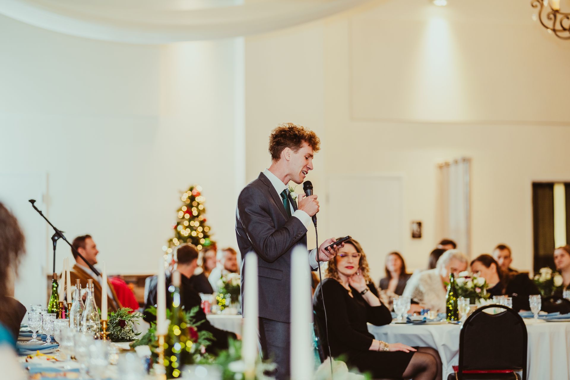 A man is standing in front of a microphone giving a speech at a wedding reception.
