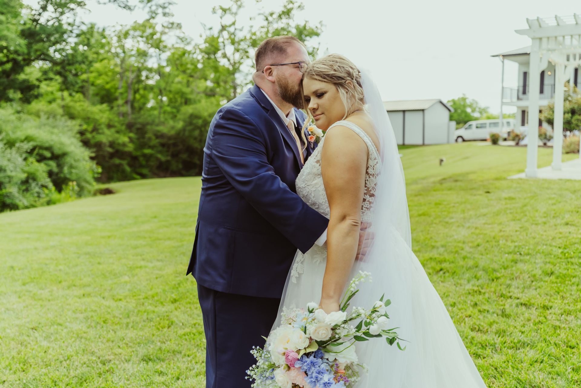 A bride and groom are kissing in a field on their wedding day.
