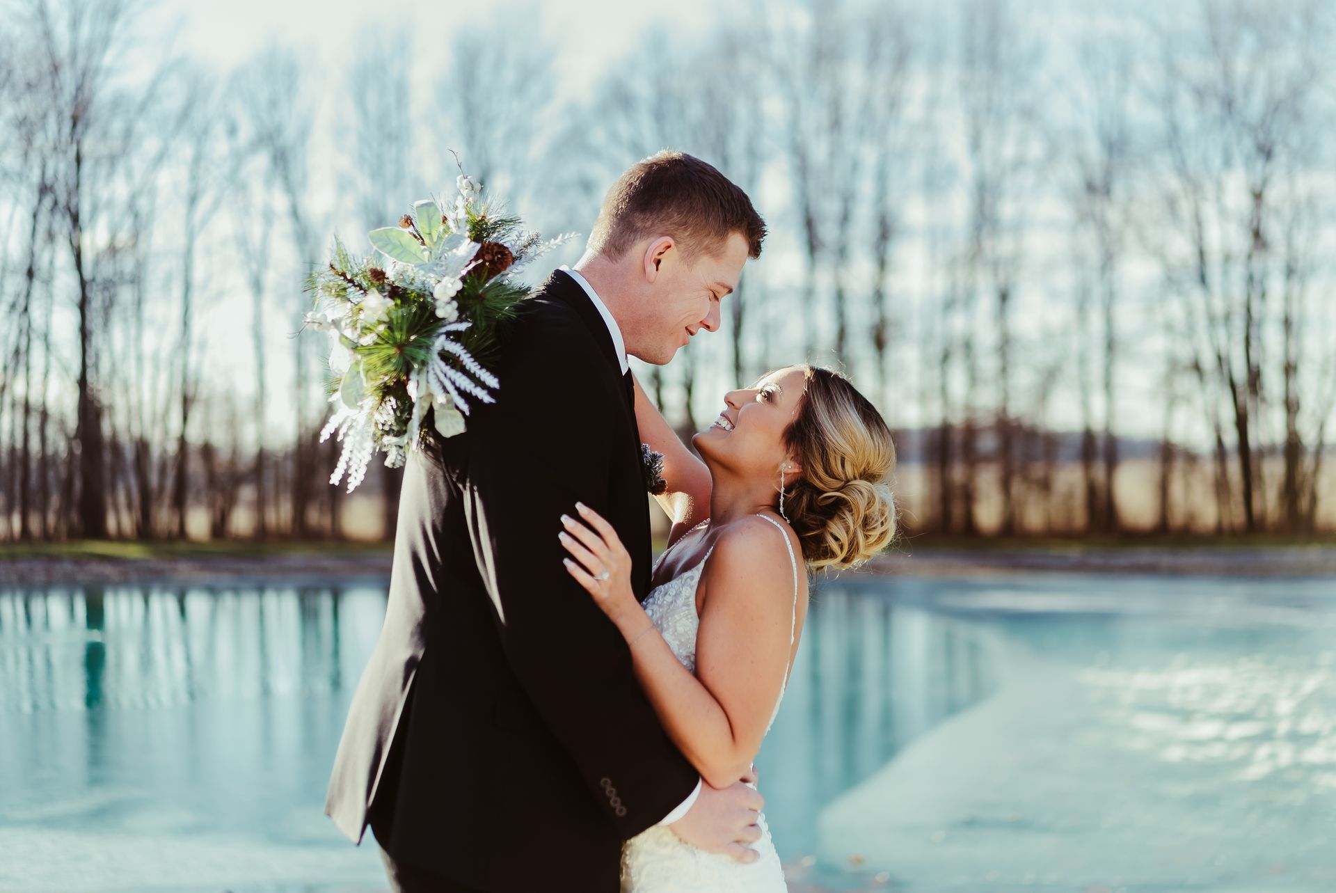 A bride and groom are posing for a picture in front of a lake.