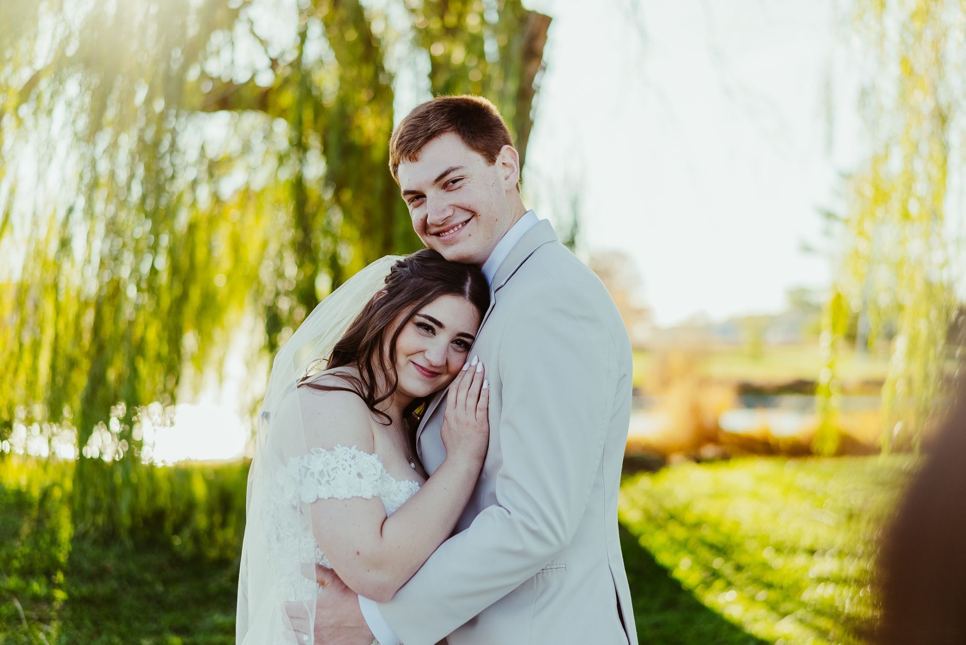 A bride and groom are posing for a picture in front of a willow tree.