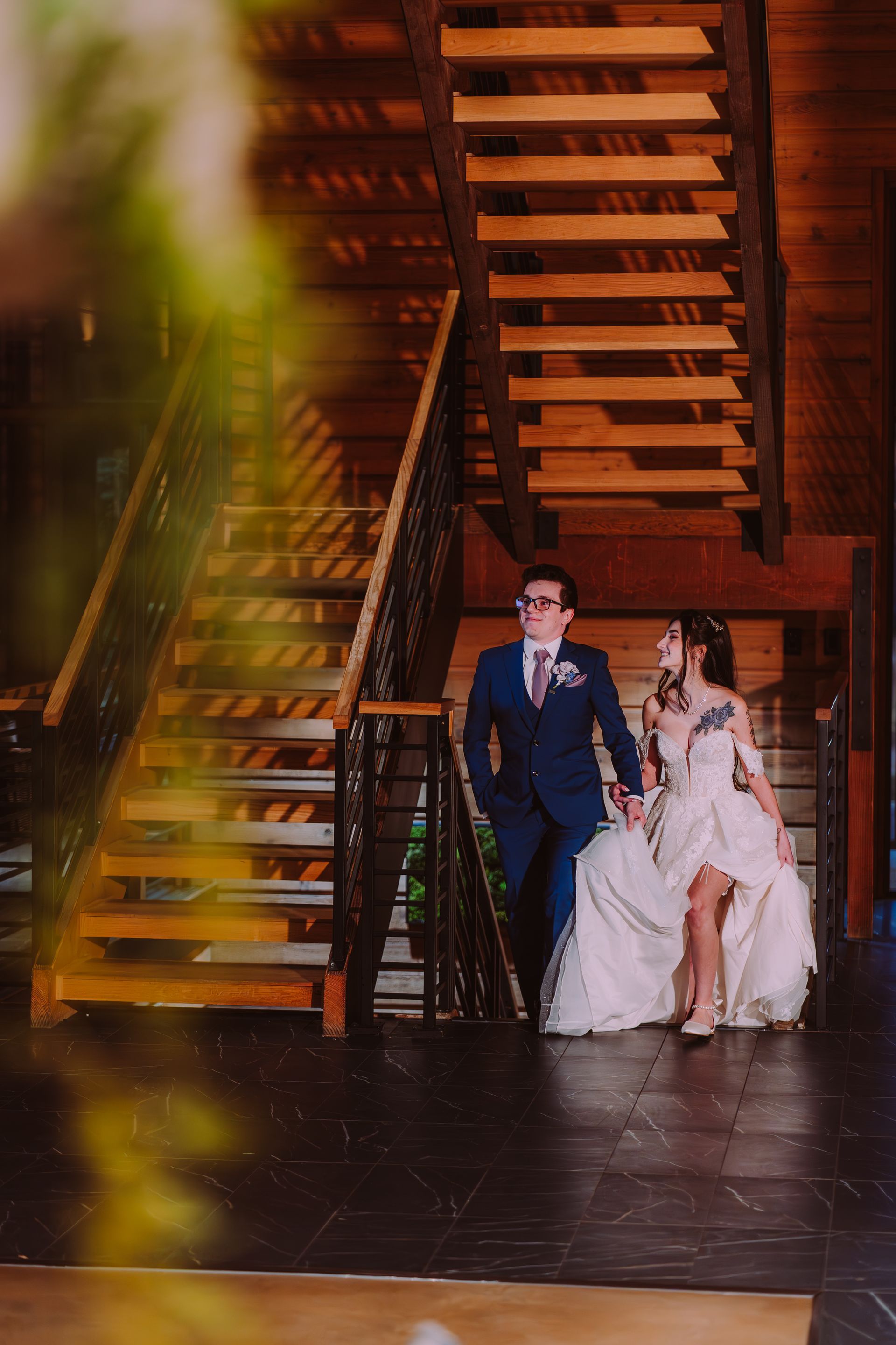 Couple in formal attire descending wooden stairs, holding hands.