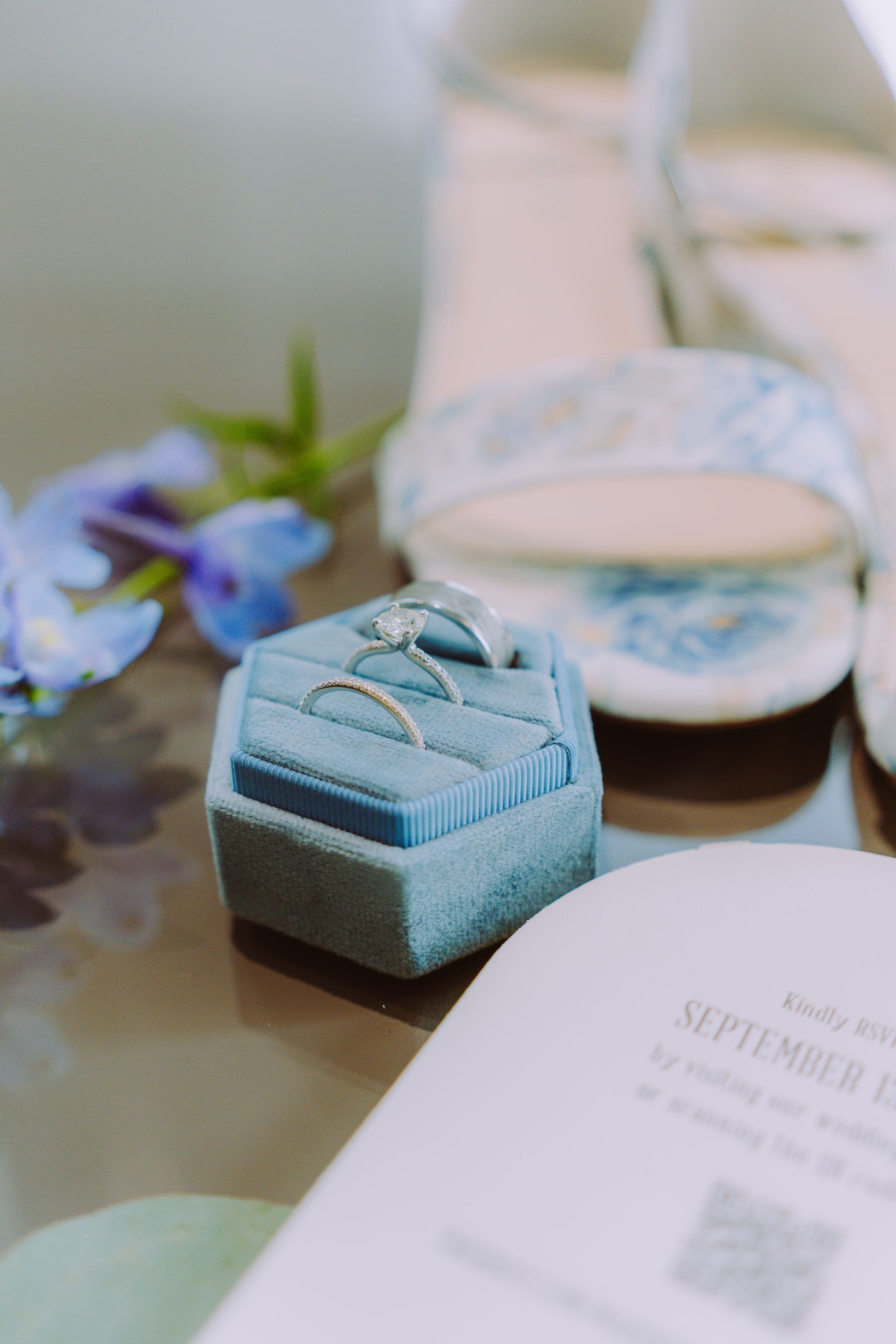 Wedding rings in a blue velvet box, with shoes, a blue flower, and wedding details.