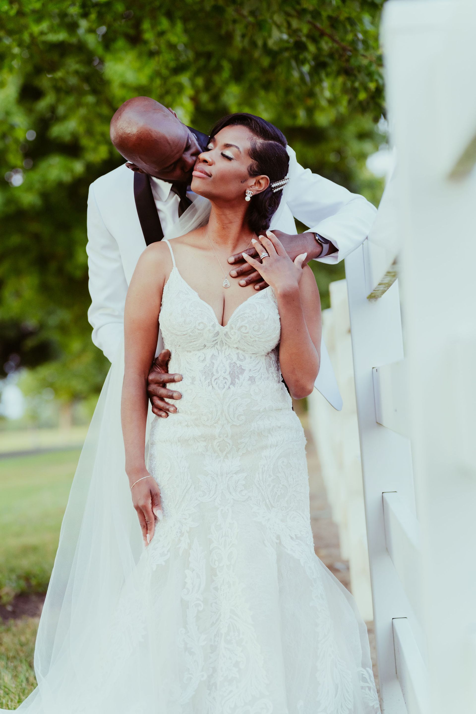 A bride and groom are posing for a picture and the groom is kissing the bride on the cheek.