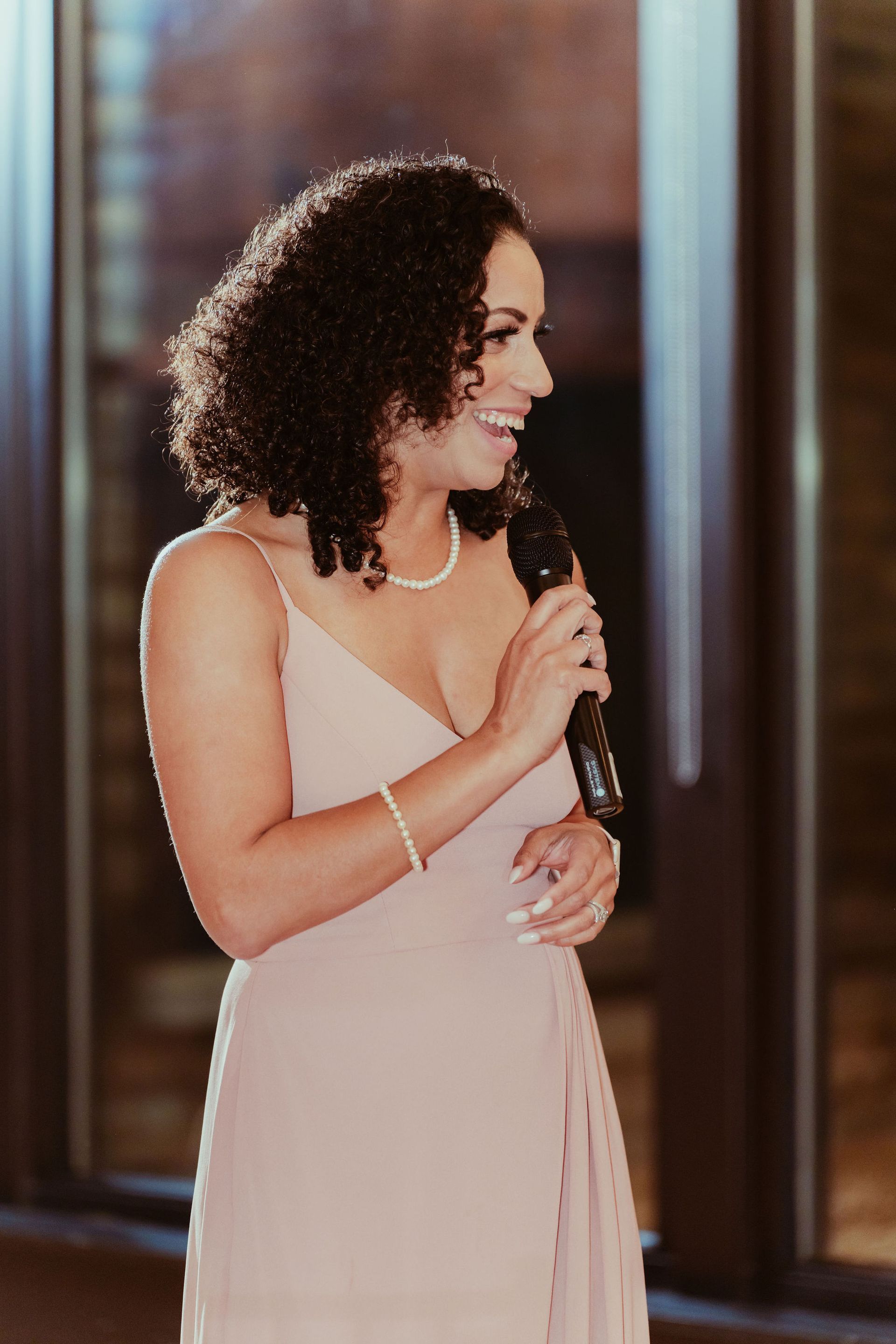 A woman in a pink dress is holding a microphone and smiling.