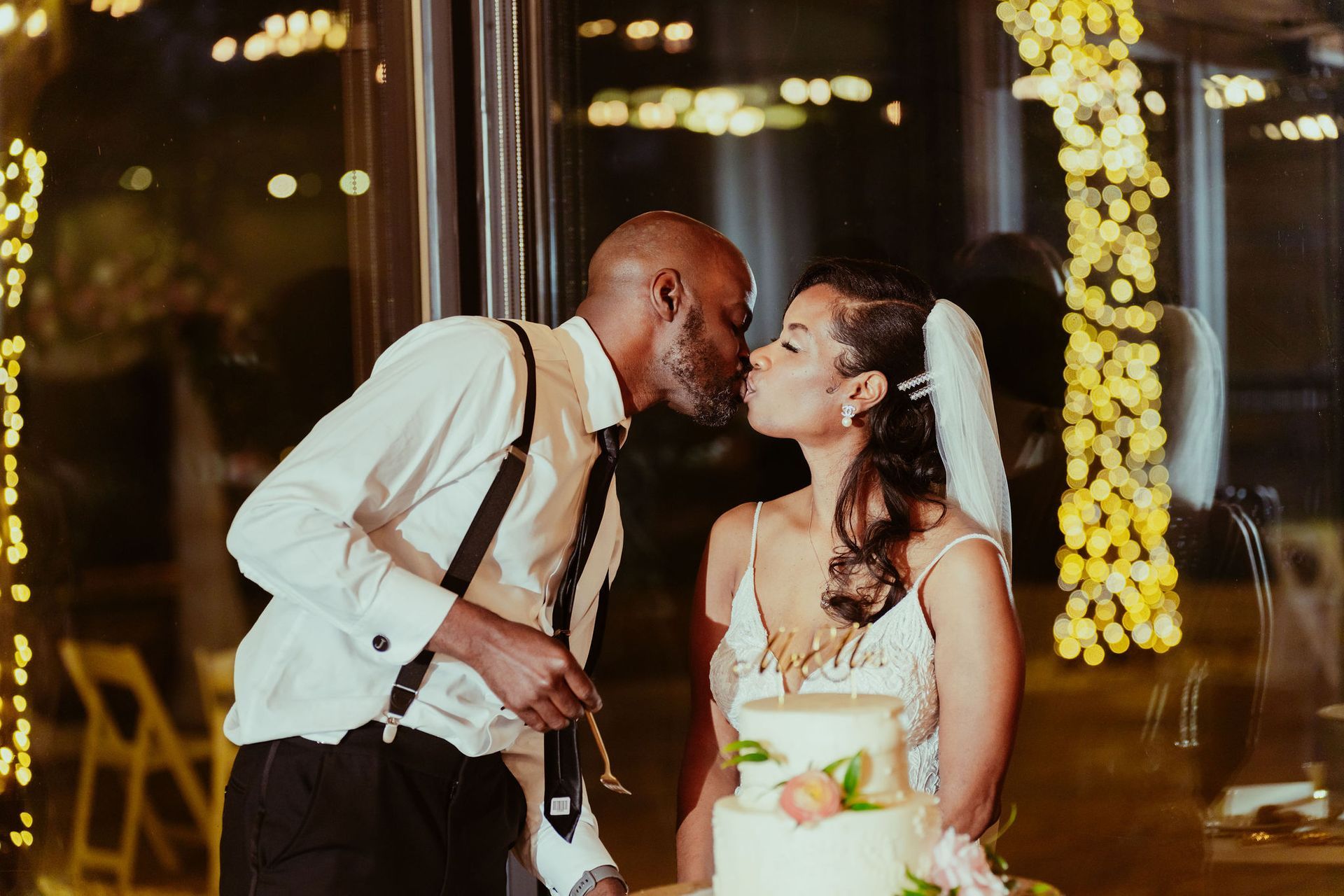 A bride and groom are kissing while cutting their wedding cake.