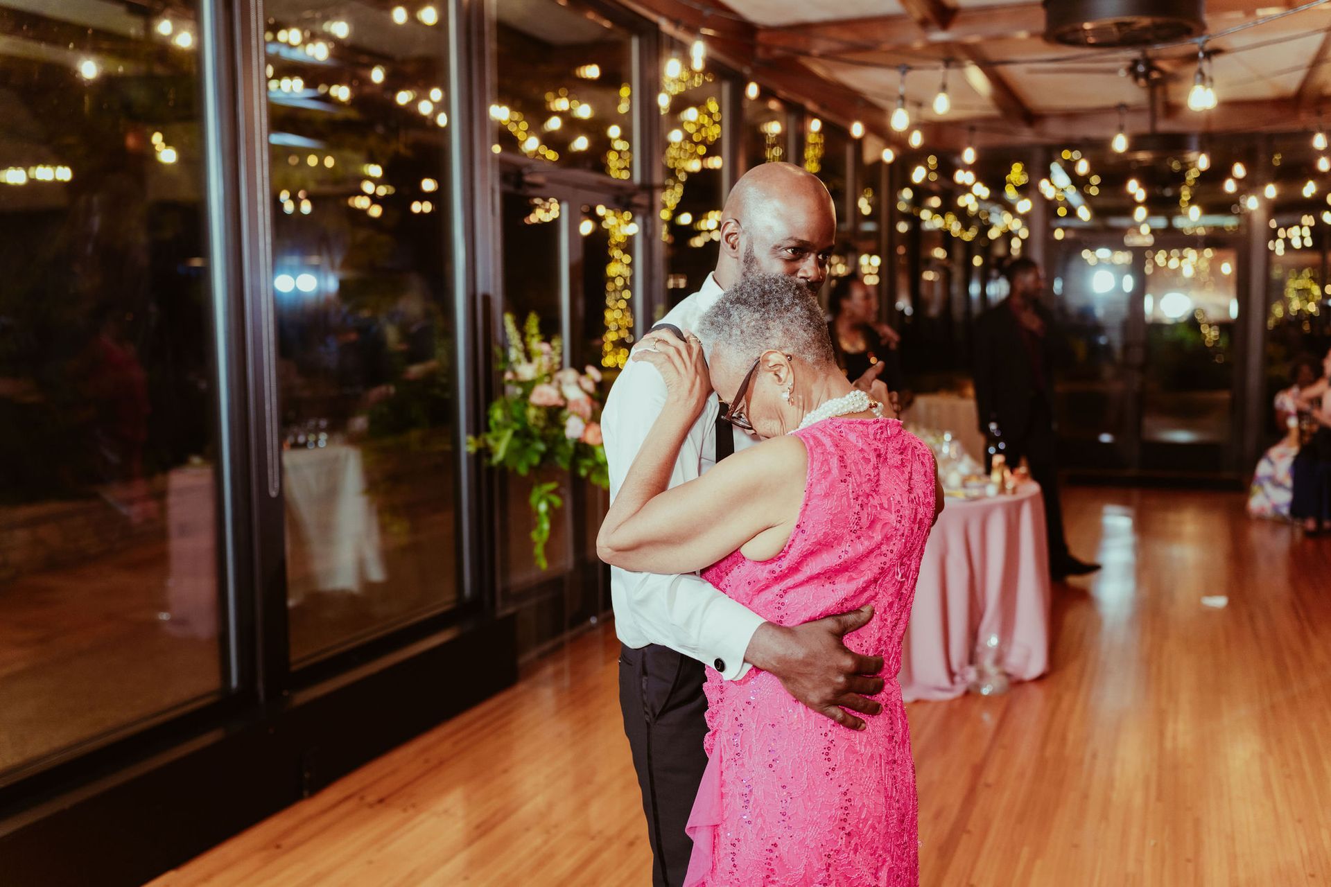 A man and woman are dancing together at a wedding reception . the woman is wearing a pink dress.