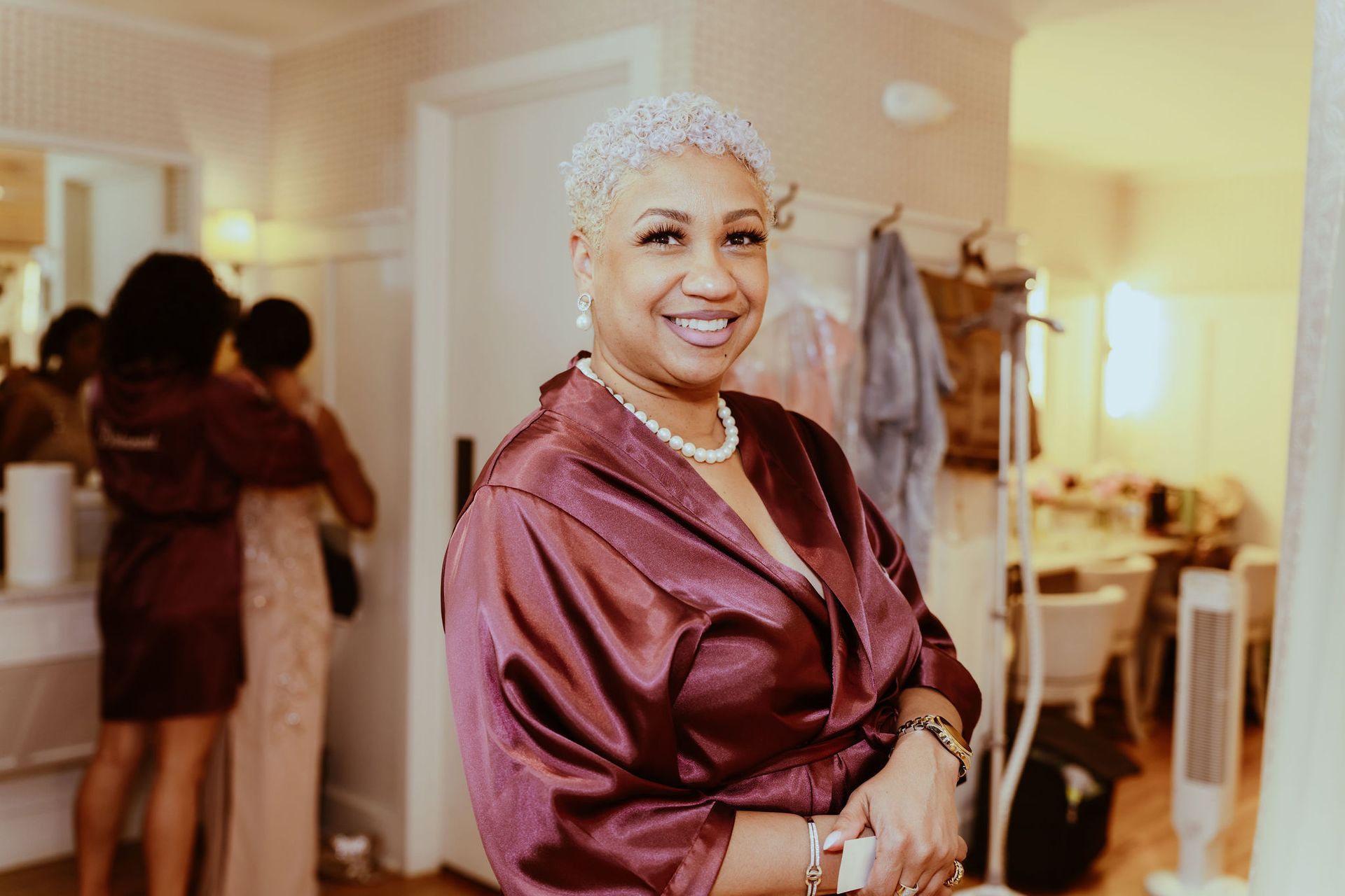 A woman in a robe is standing in a room and smiling.