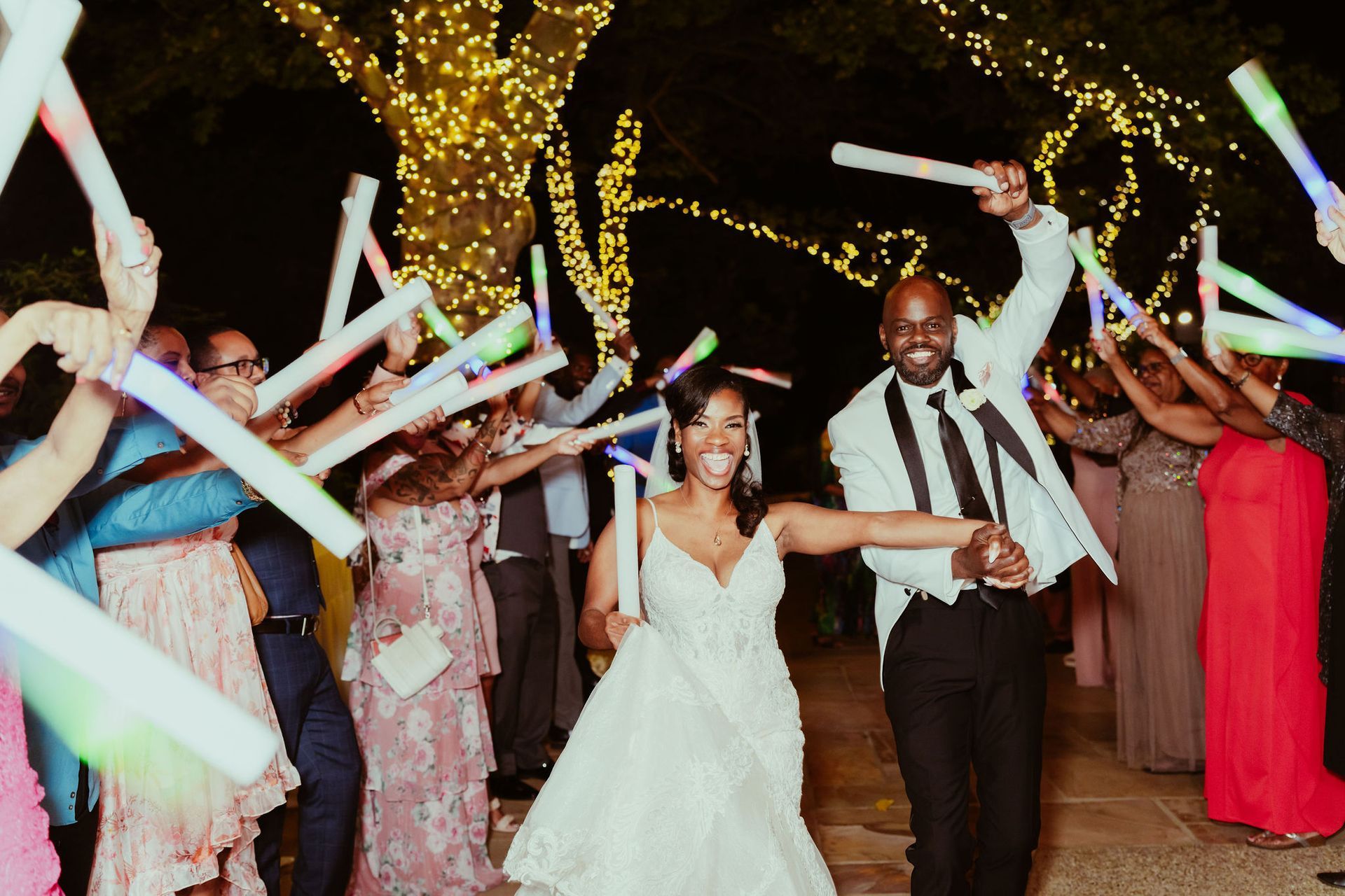 A bride and groom are walking through a crowd of people holding glow in the dark sticks.