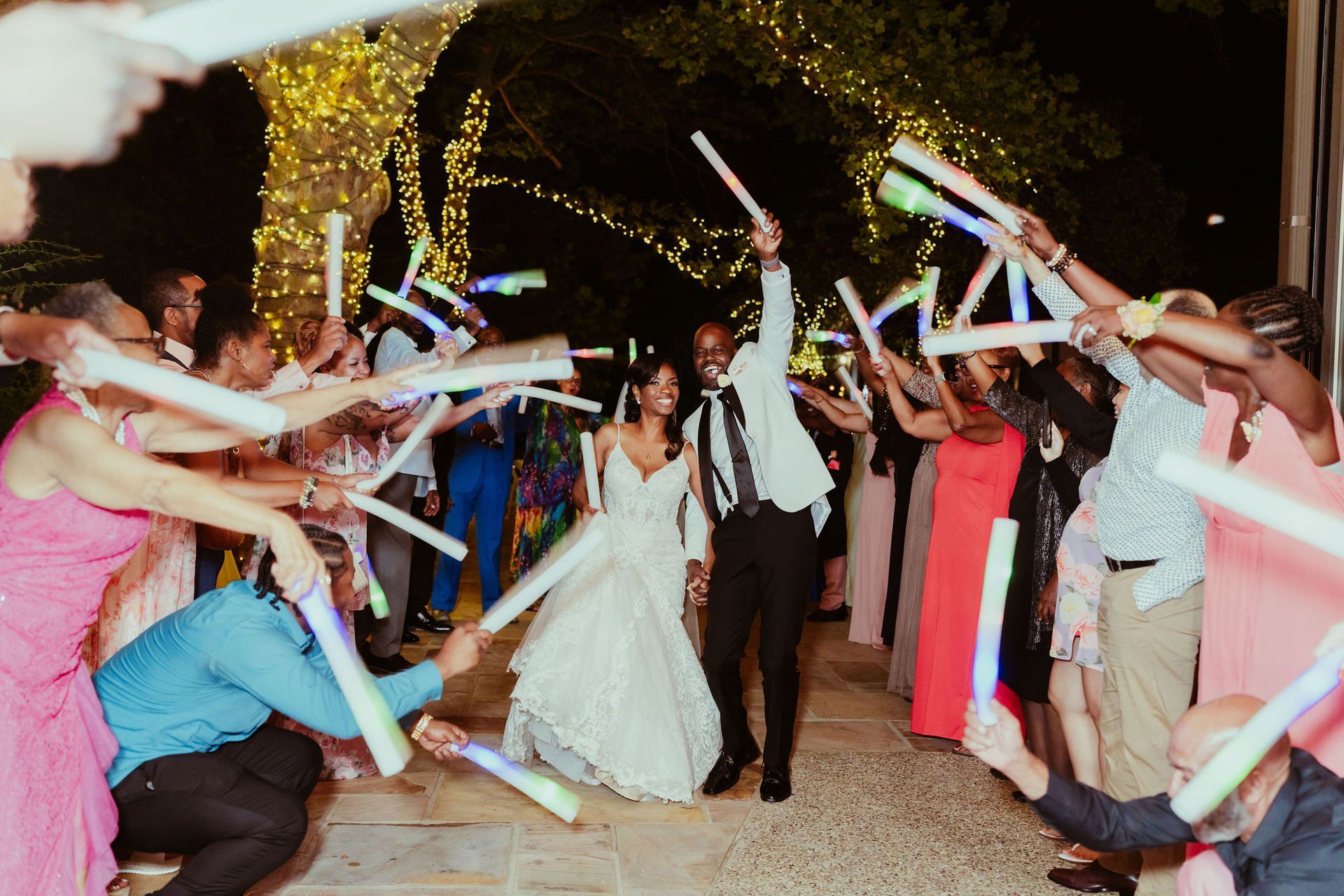 A bride and groom are walking through a crowd of people holding glow in the dark sticks.