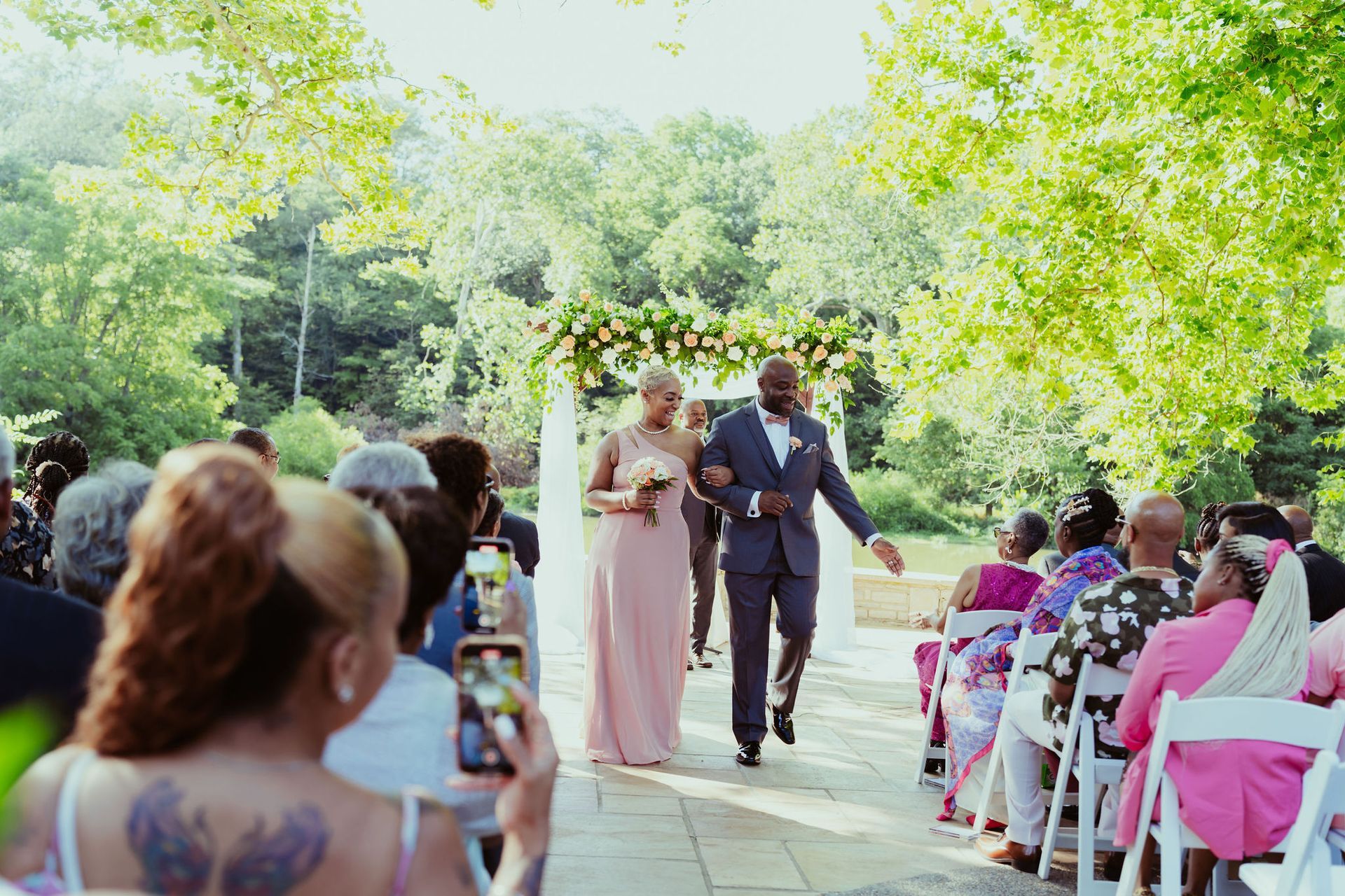 A woman is taking a picture of a bride and groom walking down the aisle at a wedding.