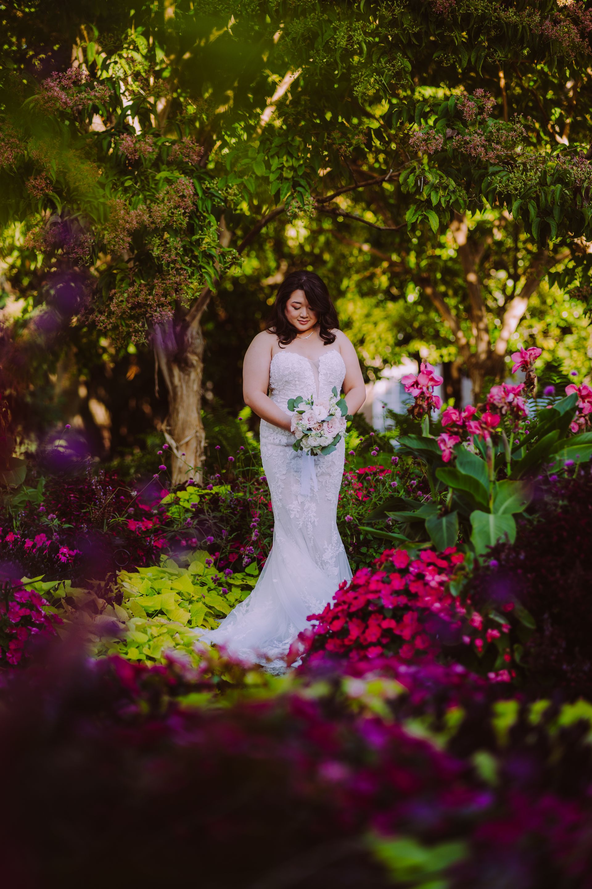 Bride in a white dress holding flowers, surrounded by colorful garden foliage.