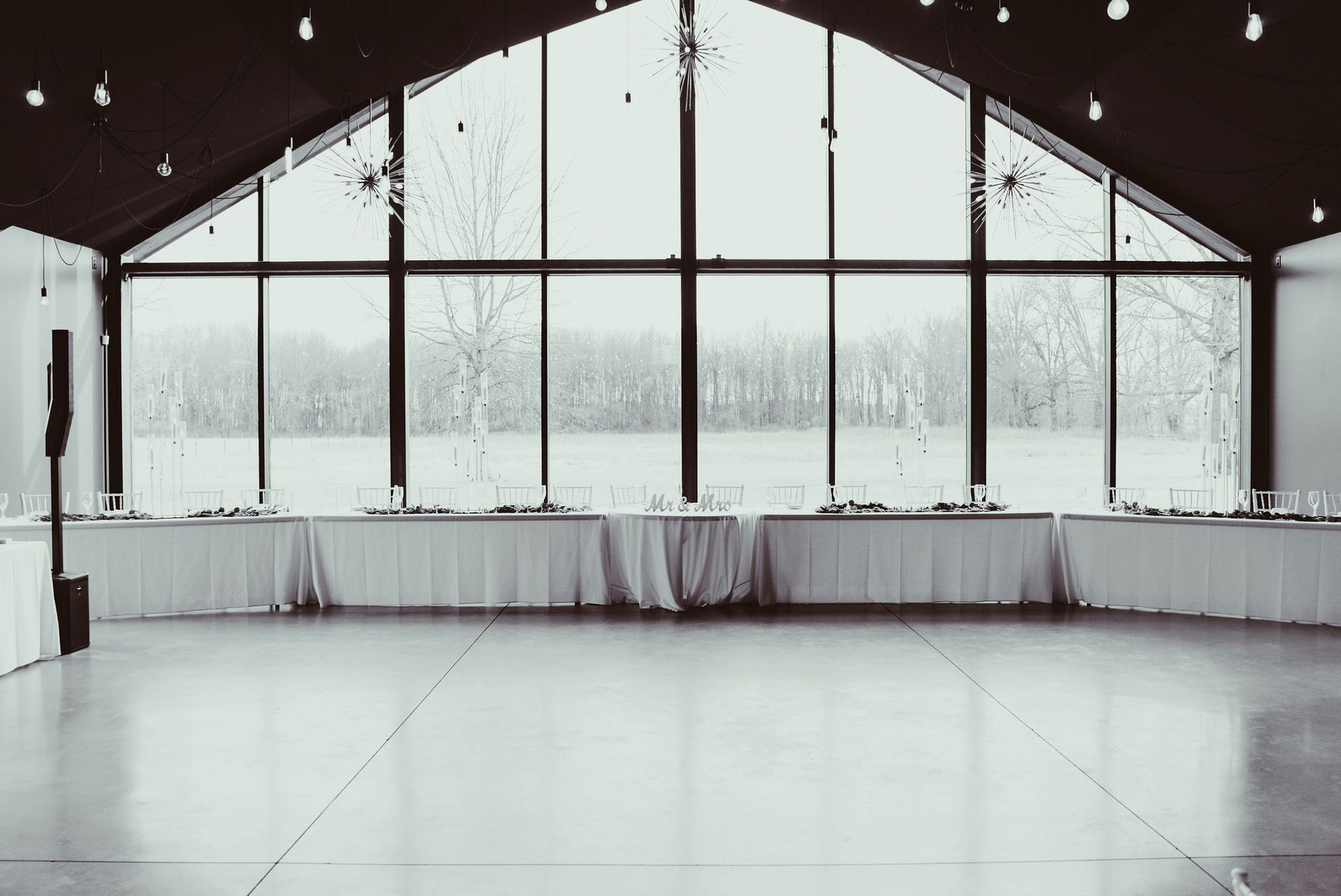 An empty dance floor in a large room with tables and a large window.