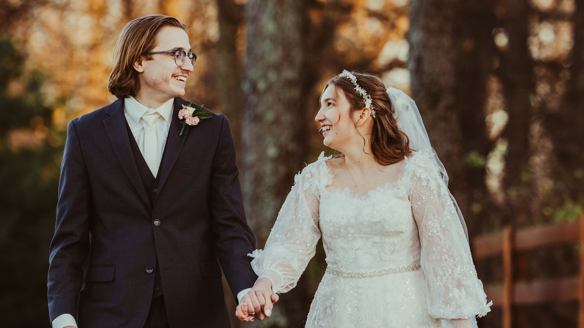 A bride and groom are holding hands while walking in the woods.