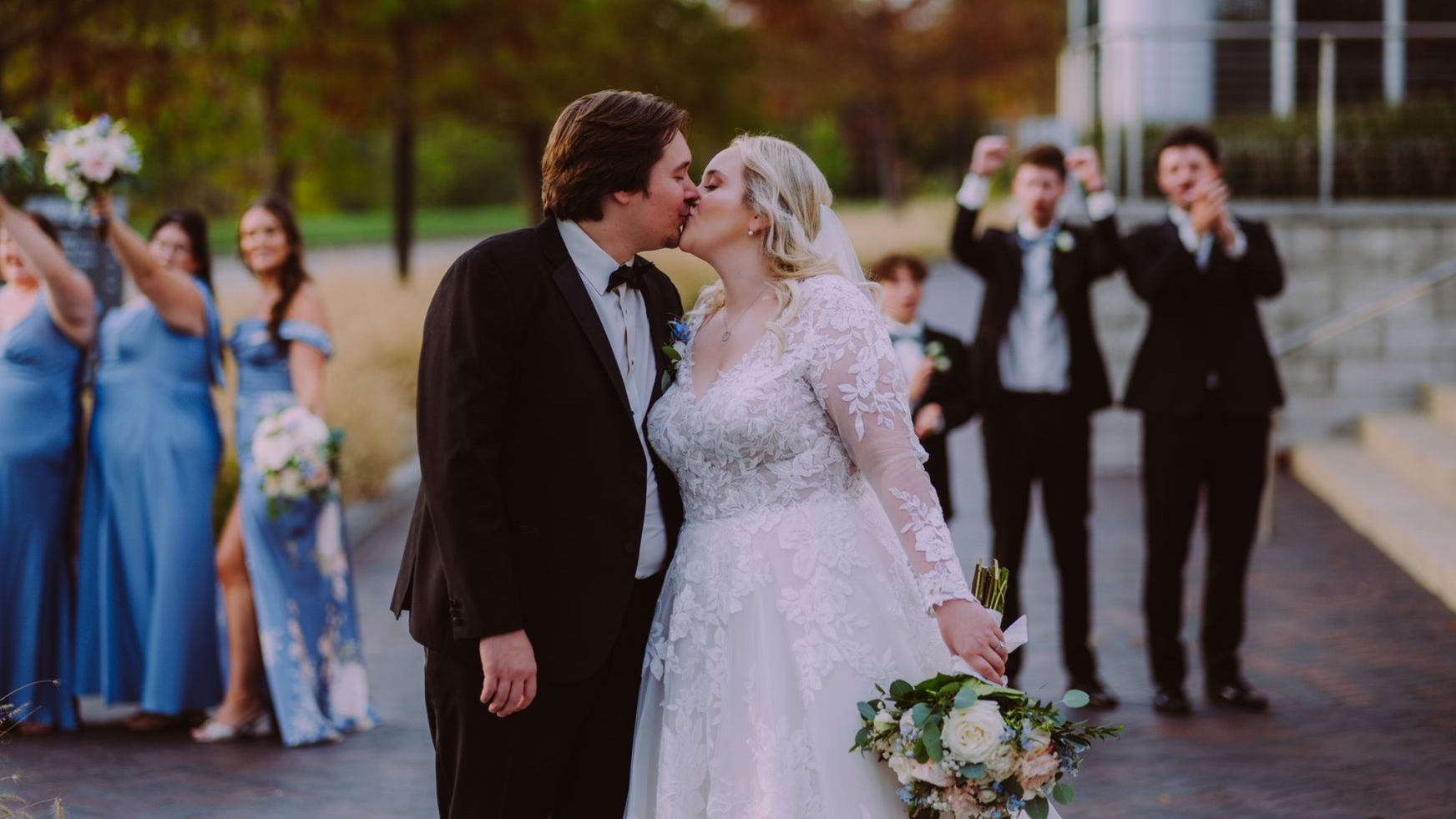 Bride and groom kissing outdoors; bridal party cheers in the background. Photo taken with A7 IV by Kodjo Somana