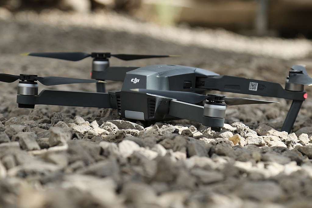 Drone on a rocky surface, gray and black, with blades extended.