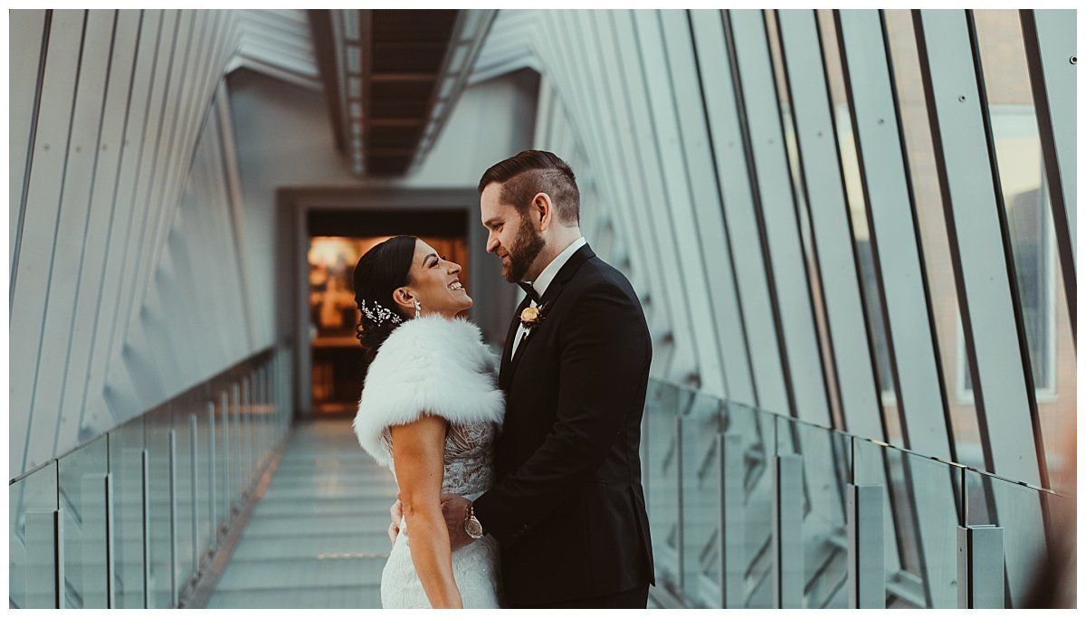 a bride and groom are standing next to each other on a bridge .