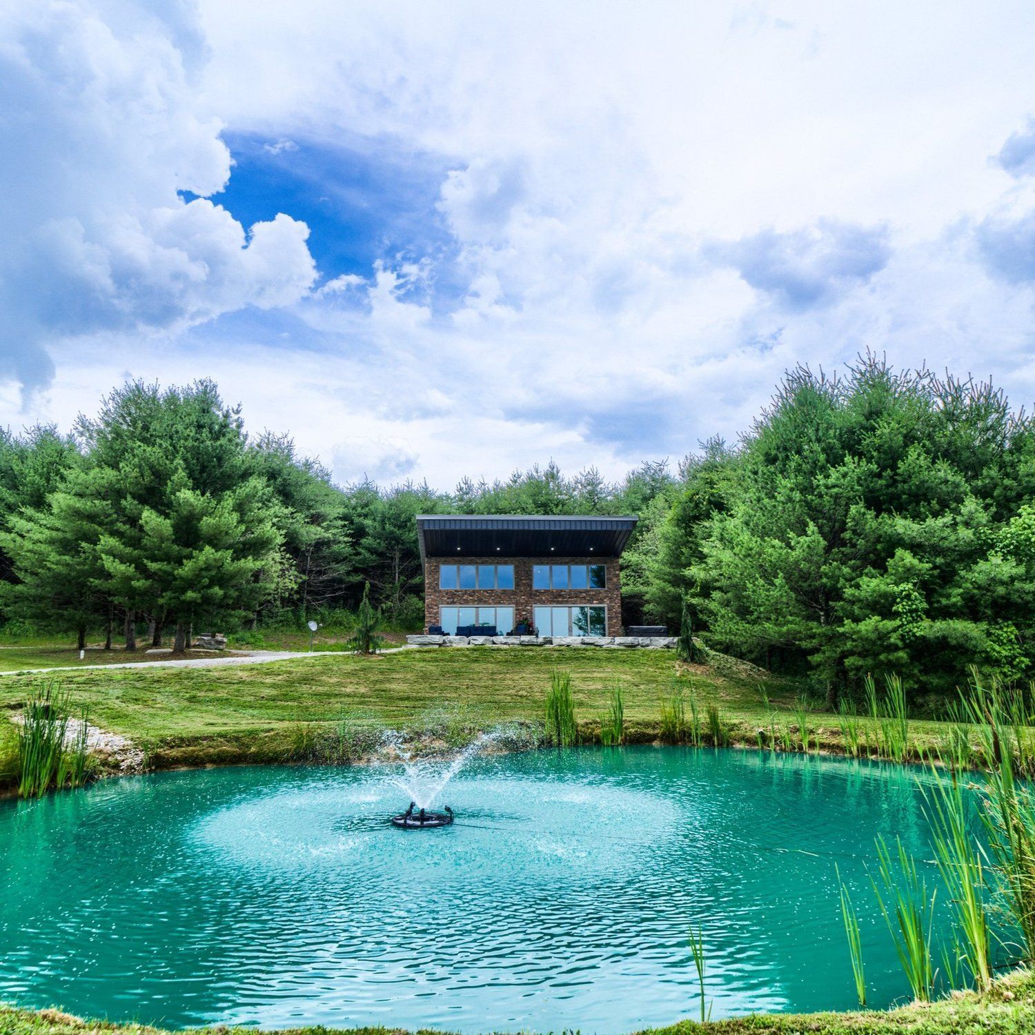 a pond with a fountain in the middle of it and a house in the background .
