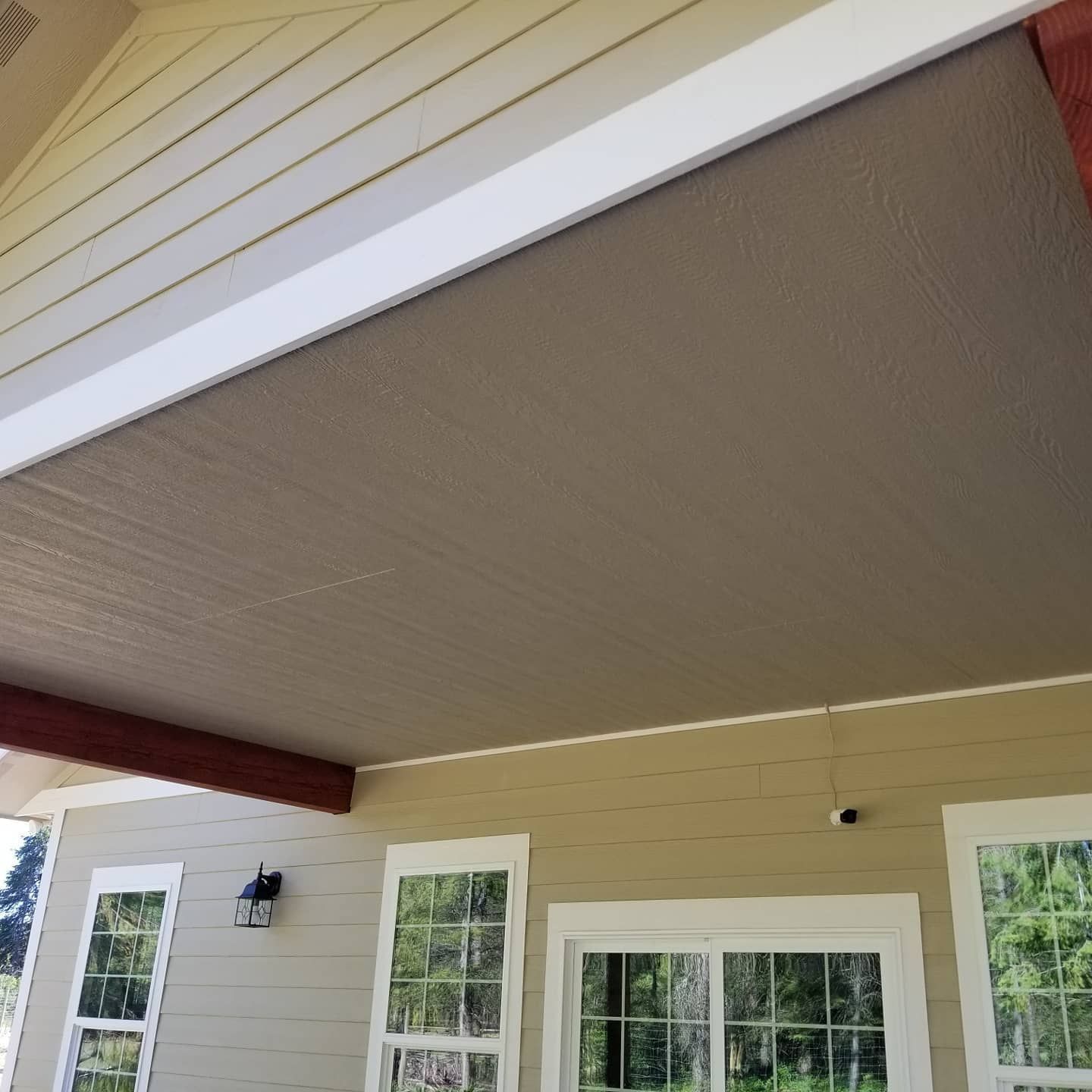 Tan porch ceiling with white trim and beige siding, windows, and brown beams.