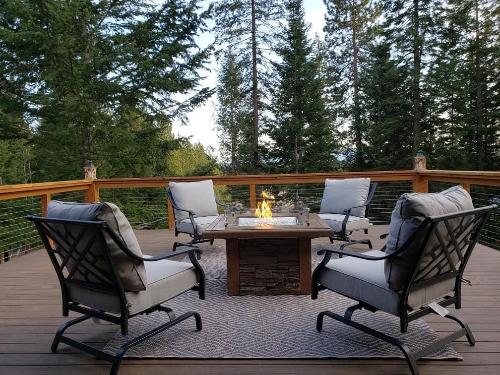 Deck with four chairs around a lit fire pit, set in a forest.