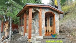 Stone and wood cottage with arched doorway, windows, and steps, surrounded by trees.
