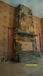 Stone fireplace under construction in a room, surrounded by unfinished walls with pink insulation.