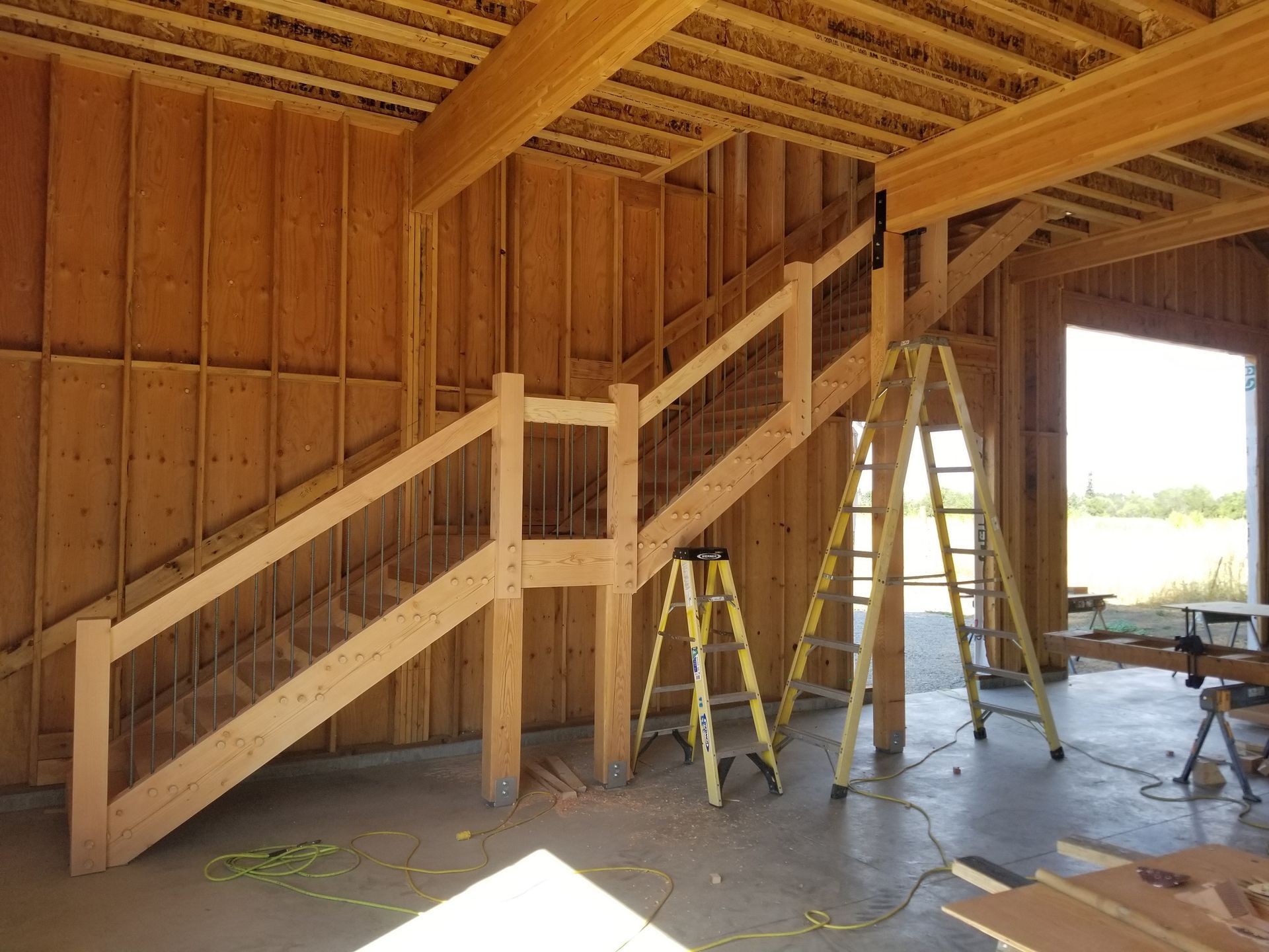 Wooden staircase under construction inside a building. Two ladders support the structure.
