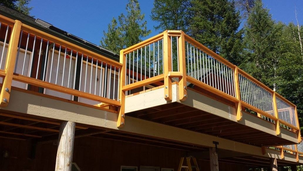 Wooden deck with gold railing and silver bars, overlooking a forest.