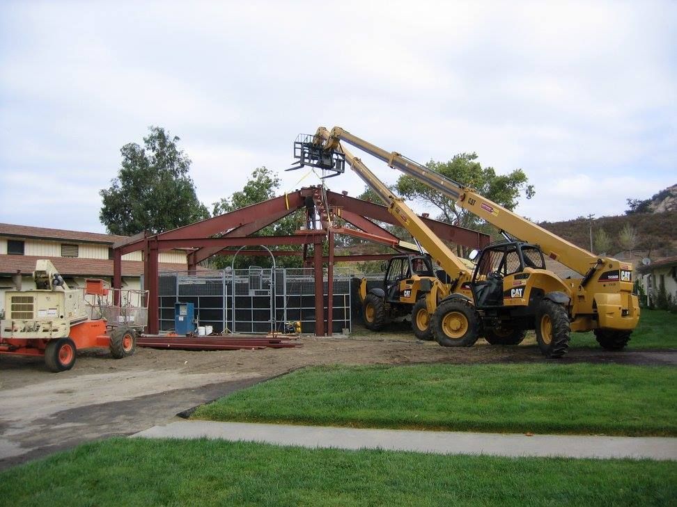 Construction site with two yellow telehandlers lifting steel beams for a building frame.
