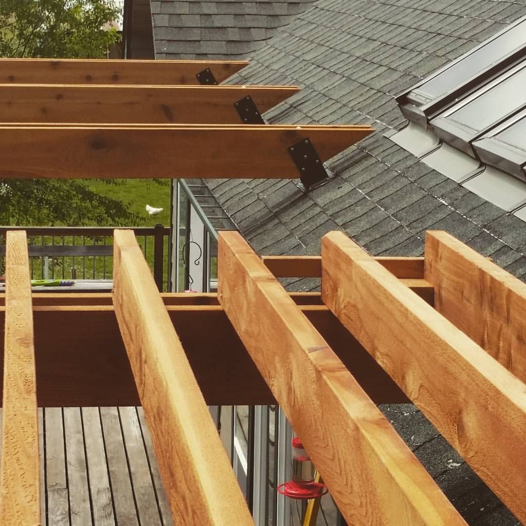 Wooden deck under construction with exposed beams, next to a gray rooftop with skylight.