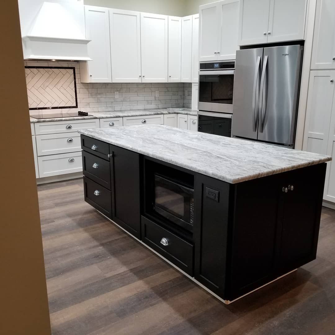 Kitchen with white cabinets, dark island with microwave, stainless steel refrigerator and light countertops.