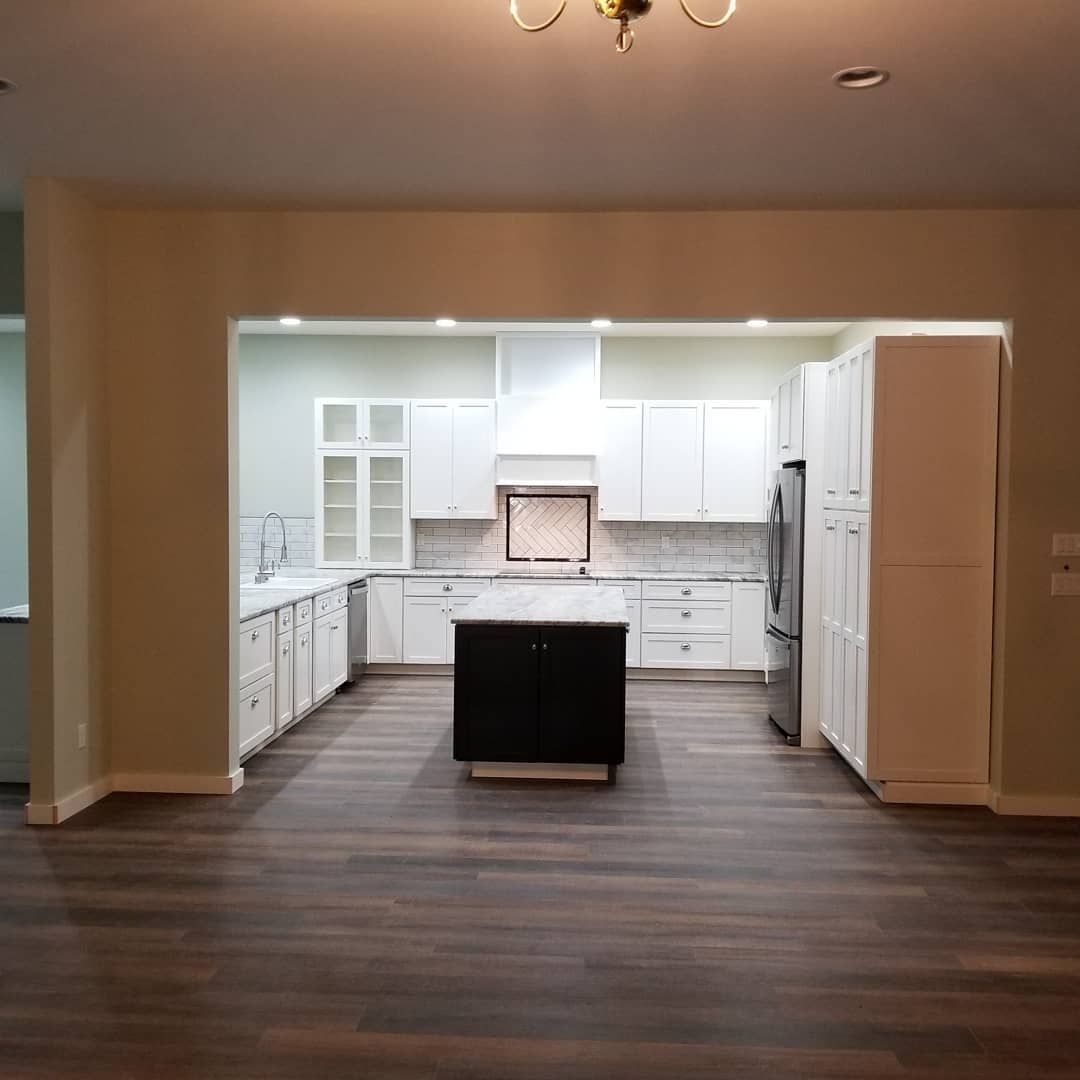 Open-concept kitchen with white cabinets, dark island, and wood-look flooring.