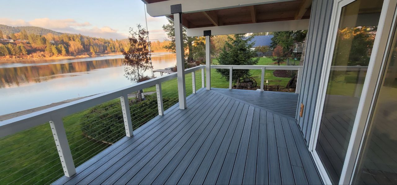 A deck with a view of a lake and mountains. The deck is gray, and the railings are white.