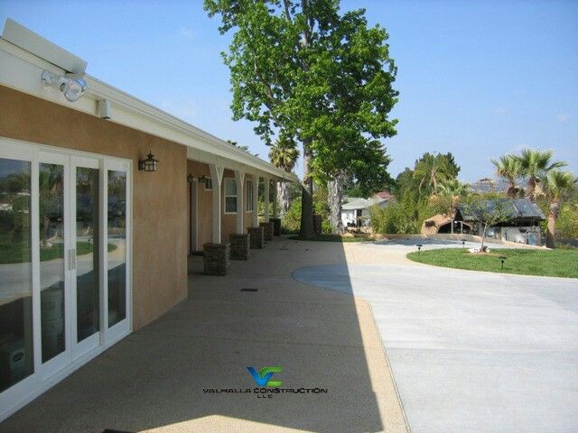 Tan building with glass doors and concrete walkway on a sunny day. Trees and other buildings are visible.