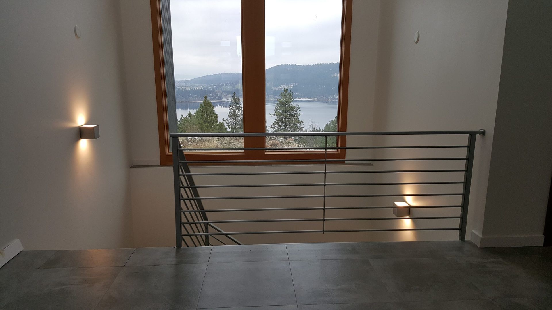 Interior view of a staircase with metal railing and window overlooking a lake and trees.