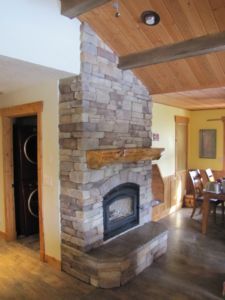 Stone fireplace in a rustic room with wooden ceiling and trim.