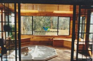 Sunroom interior with hot tub, wood features, large windows, and outdoor view.